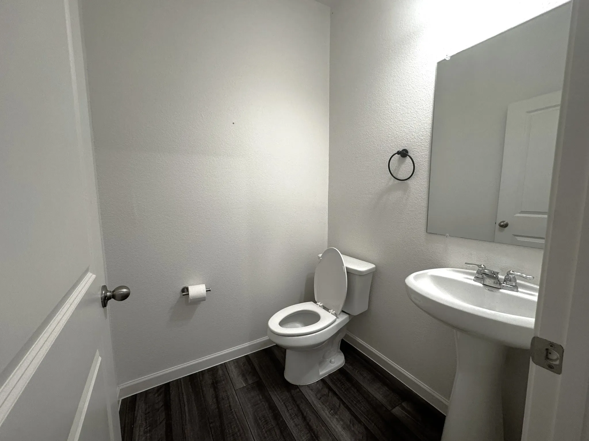Interior powder room featuring wood-finish flooring, a white pedestal sink with chrome faucet, and a large wall-mounted mirror