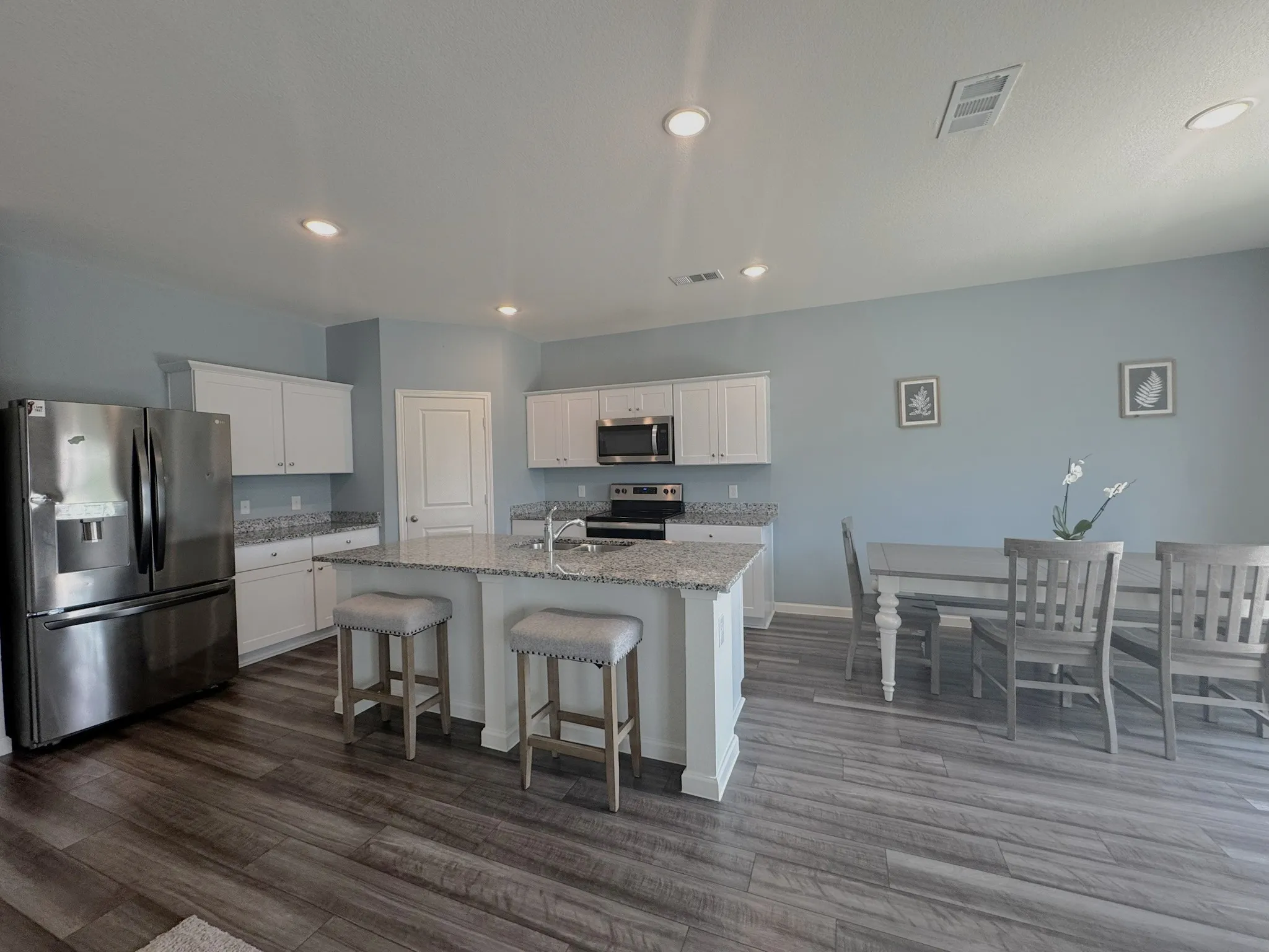 Kitchen and dining area featuring wood-finish flooring, white cabinetry, a kitchen island with seating, recessed lighting, and a stainless steel appliance suite