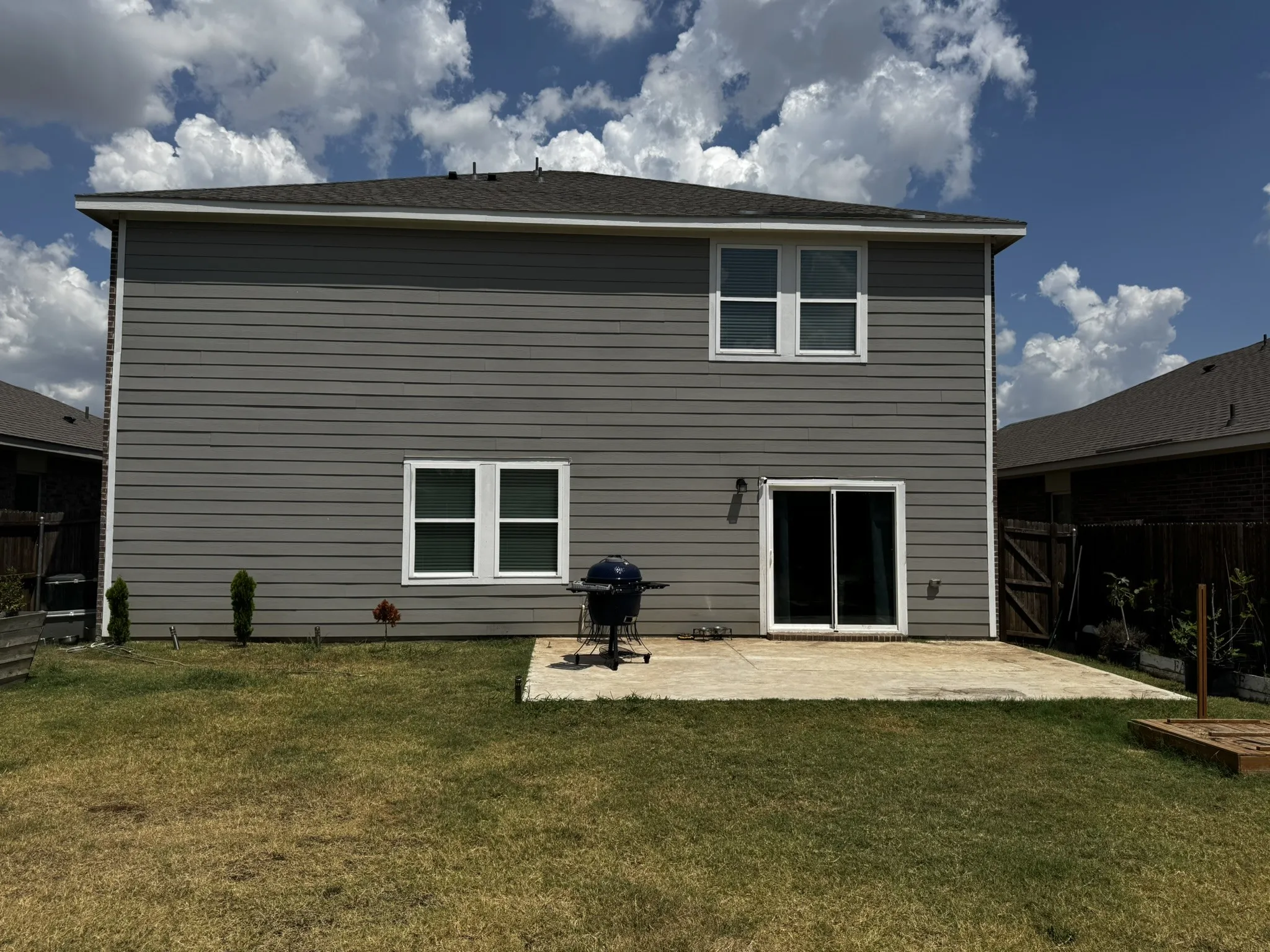 Rear exterior featuring gray horizontal siding, white trim, a concrete patio, and a sliding glass door
