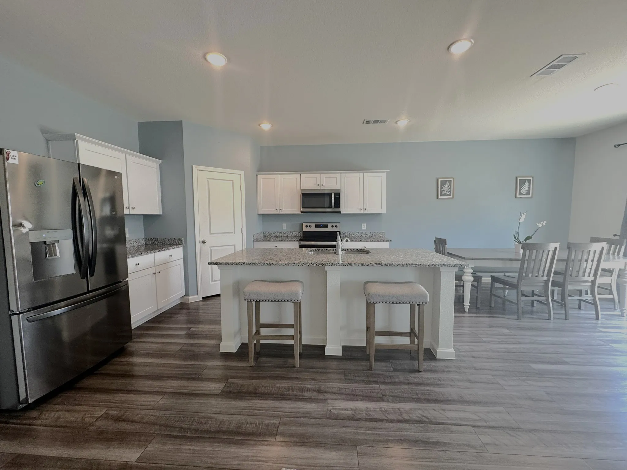 Spacious kitchen featuring an expansive island with seating, white shaker cabinetry, stainless steel appliances, and wood-finish flooring