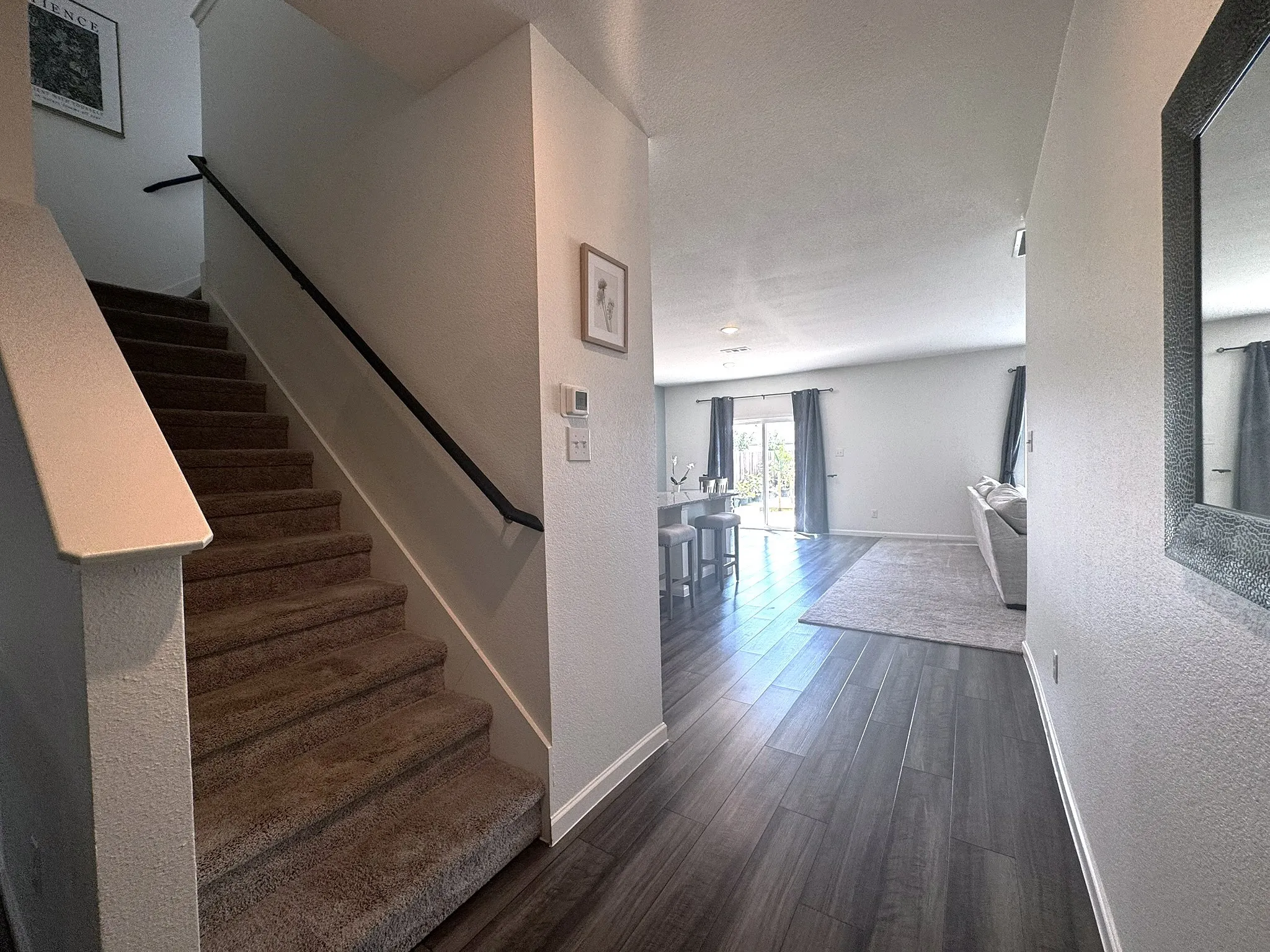 Carpeted staircase with a dark handrail, complemented by wood-finish flooring extending into the living area