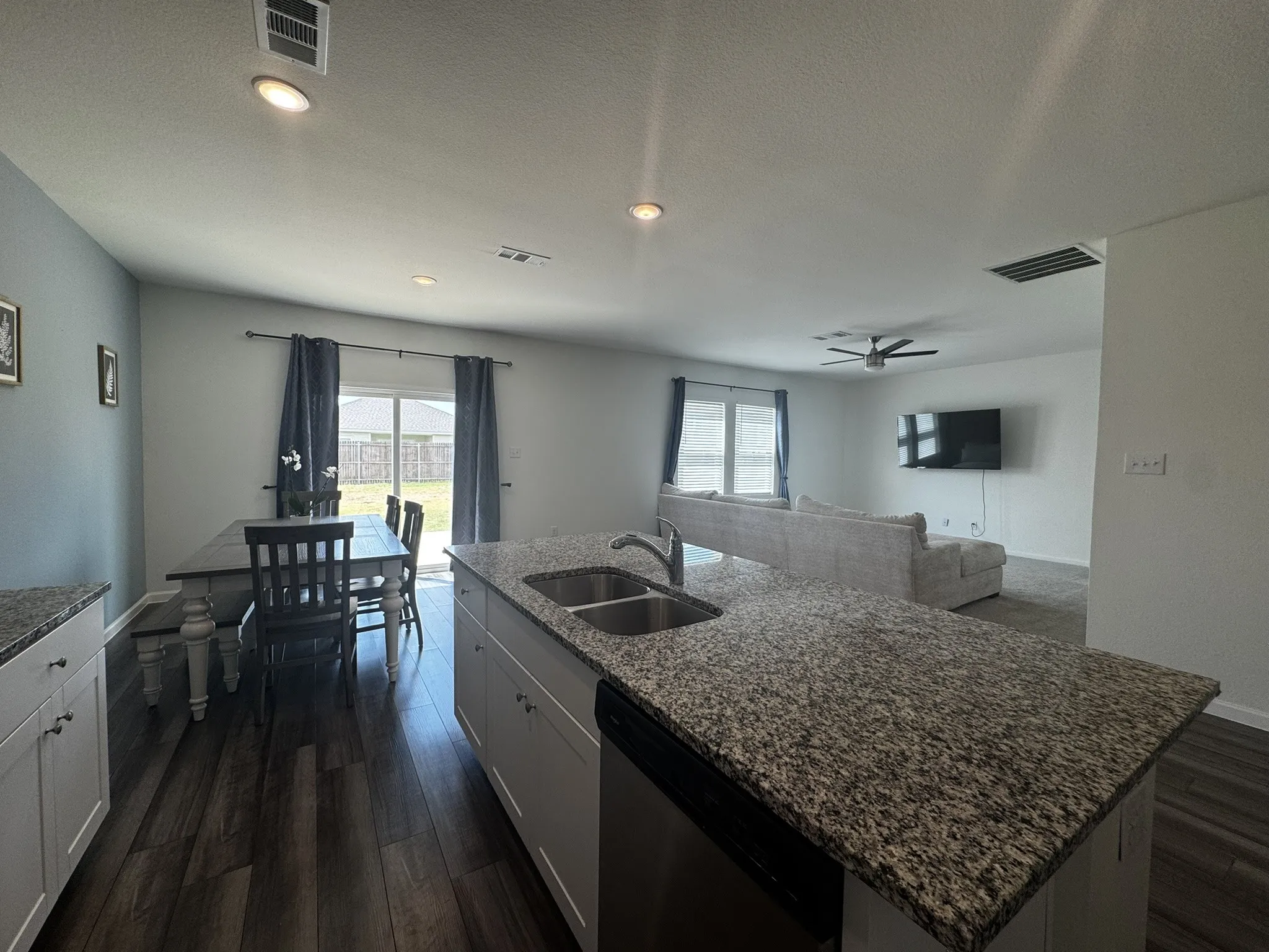 Open-concept kitchen featuring an island with a double basin sink, granite-style countertops, white cabinetry, and wood-finish flooring