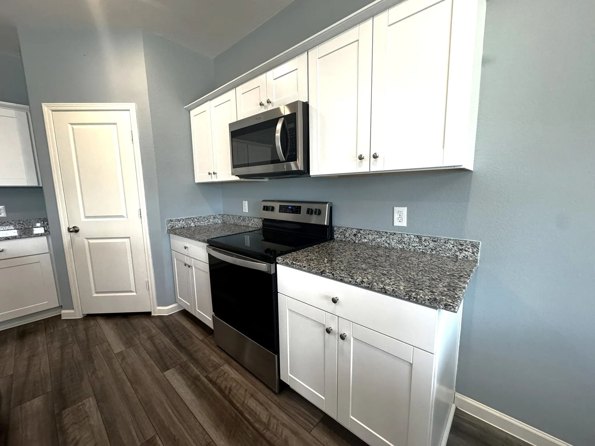 Contemporary kitchen featuring white shaker cabinetry, granite-style countertops, stainless steel appliances, and wood-finish flooring