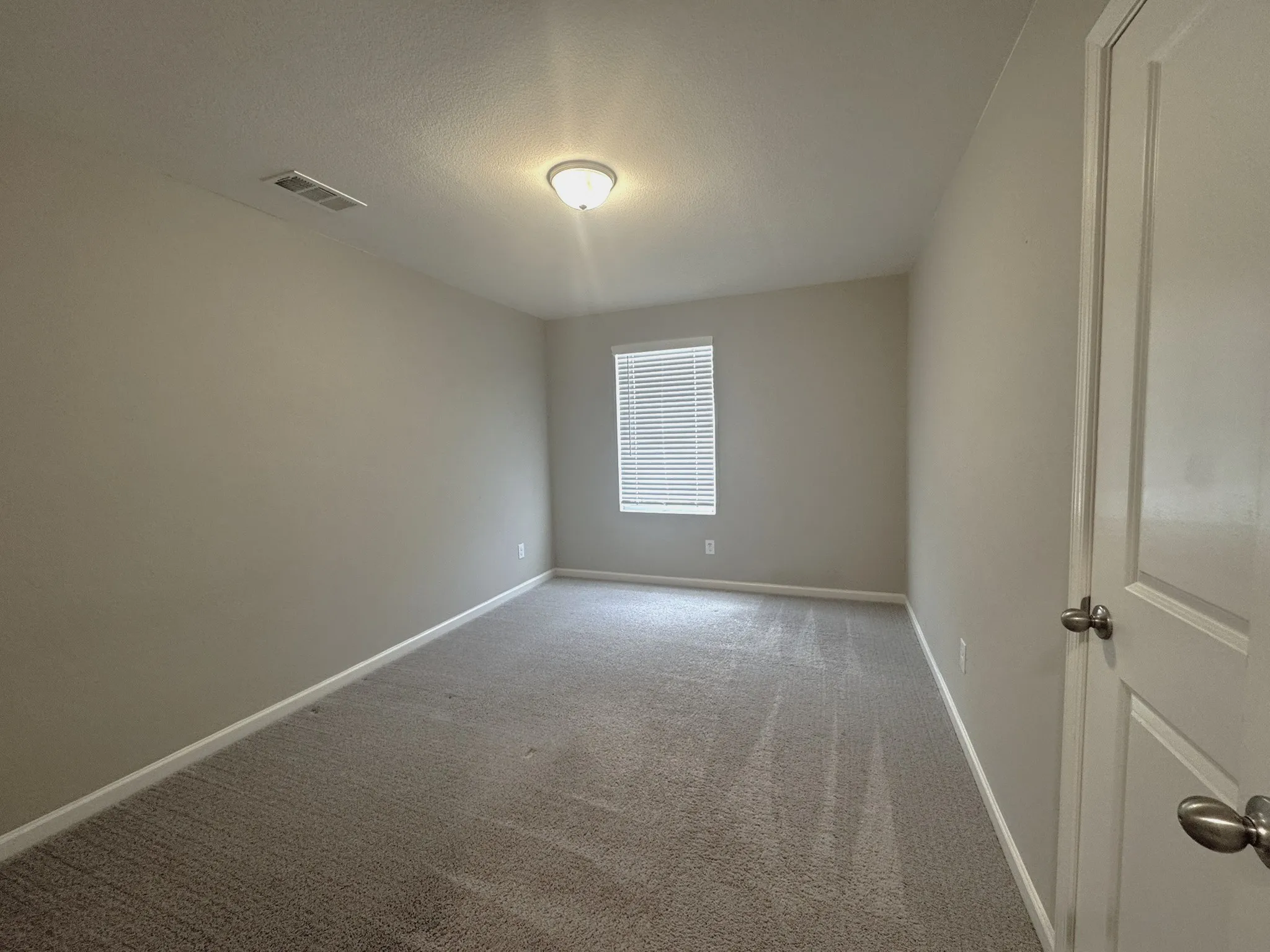 Carpeted room with a single window, overhead flush-mount lighting, and light neutral wall paint