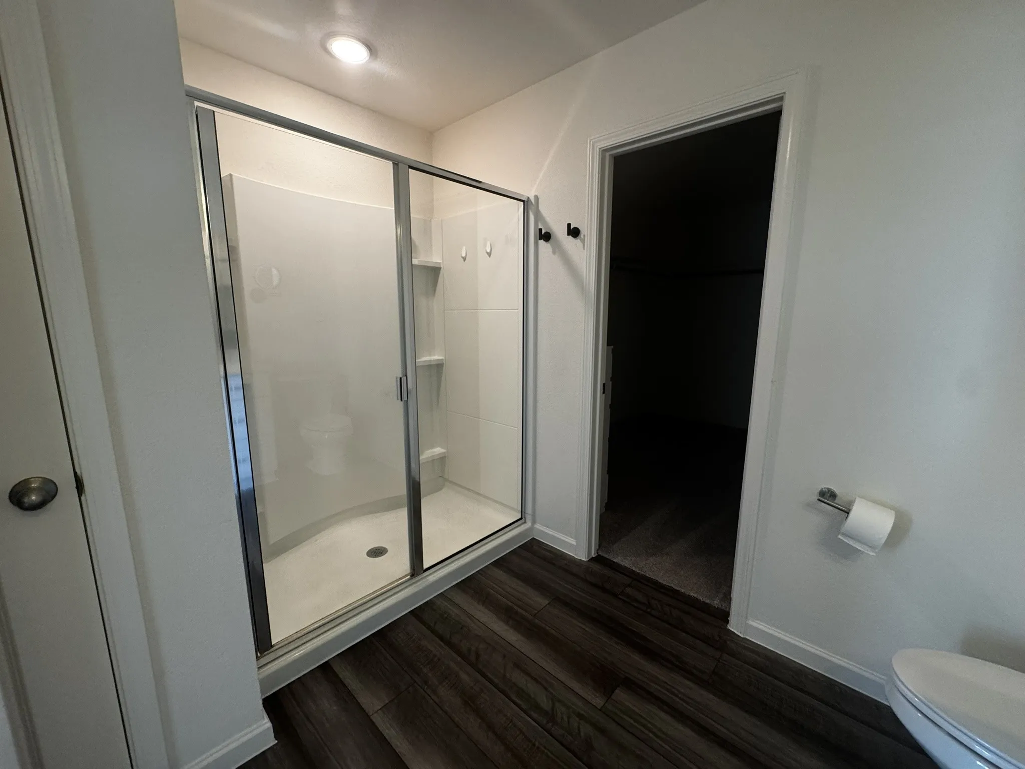 Glass-enclosed shower with white acrylic surround, built-in shelving, and a chrome-finish shower head