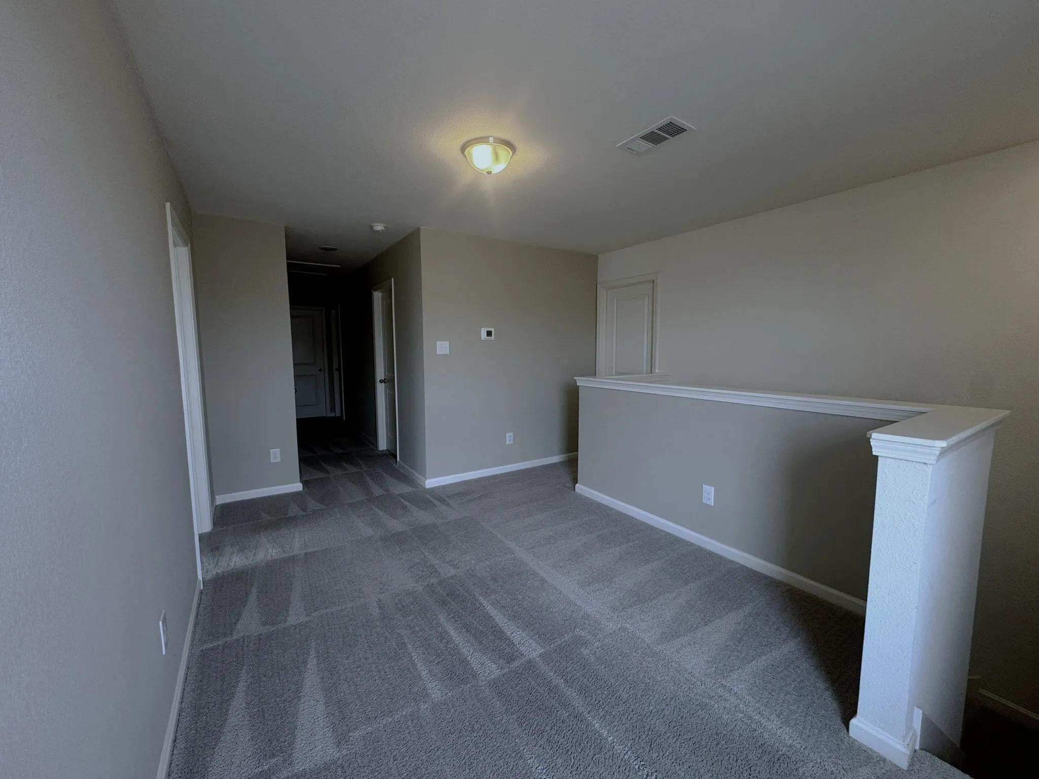 Carpeted upstairs landing featuring a neutral color palette, white trim, a flush mount ceiling light, and a half-wall railing