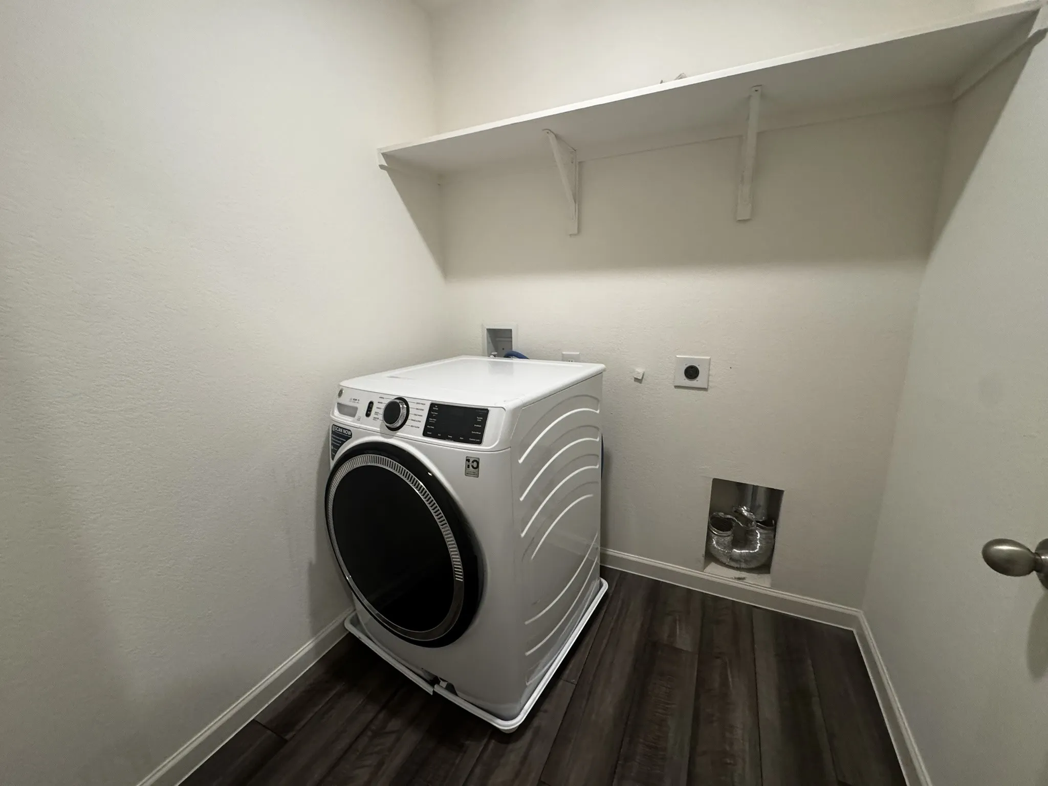Dedicated laundry area featuring wood-finish flooring, white baseboards, and a single wall-mounted shelf
