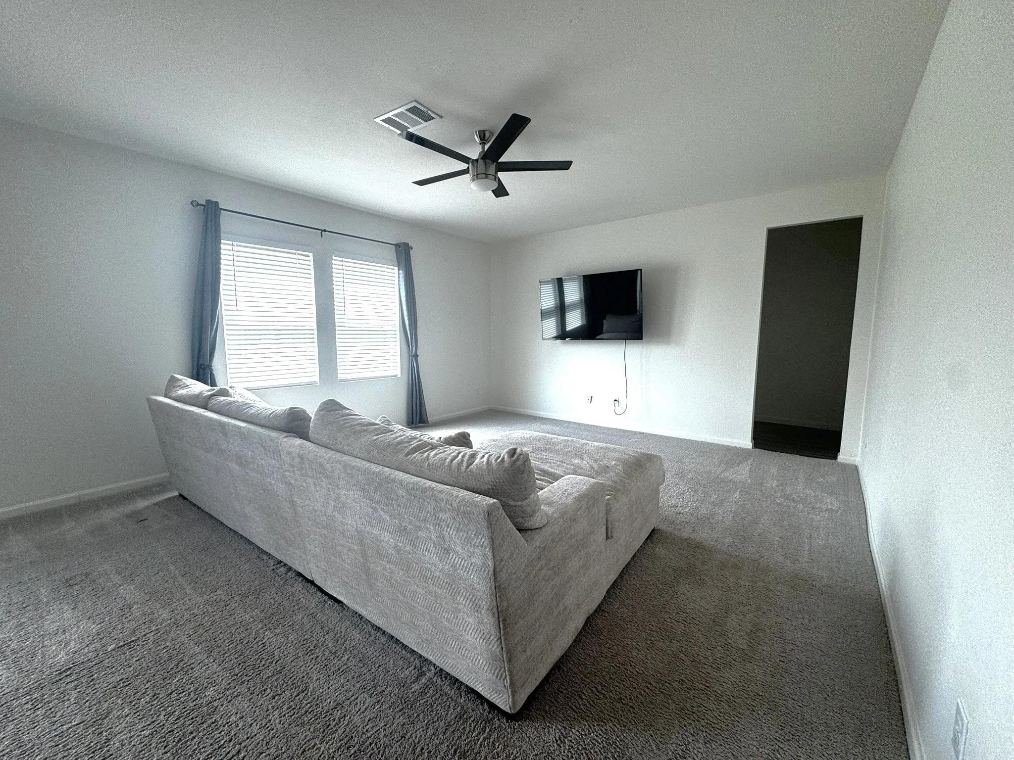 Spacious room featuring neutral carpeting, a modern ceiling fan, and white walls