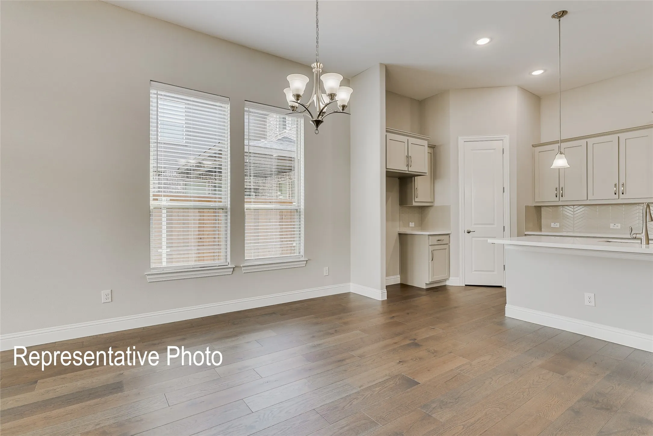 Open-concept interior featuring wood-finish flooring, two large windows with blinds, a five-light chandelier, a kitchen island with pendant lighting, and light-toned cabinetry