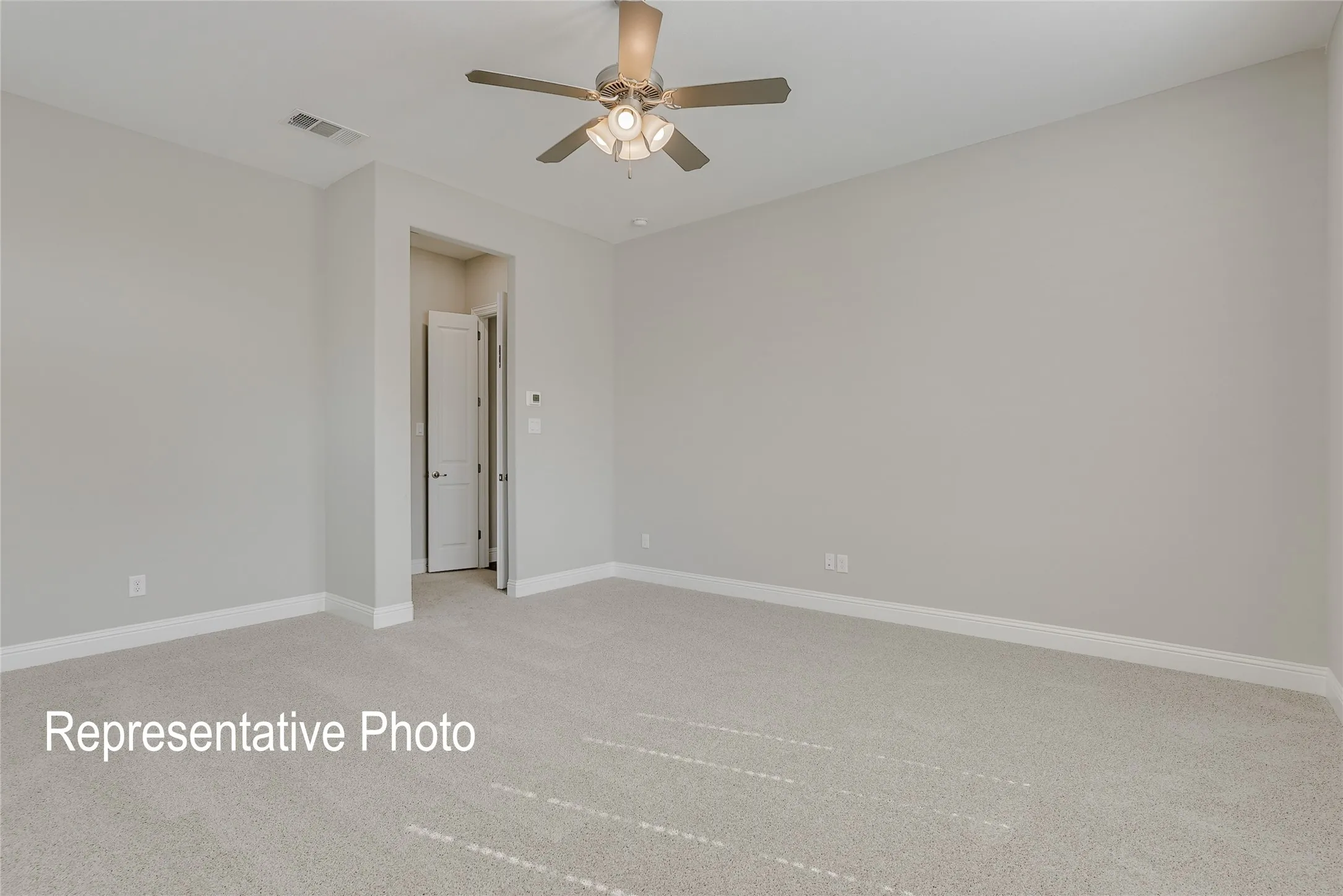 Spacious room featuring neutral carpeting, light gray walls, a ceiling fan with integrated lighting, white baseboards, and a doorway with a white paneled door
