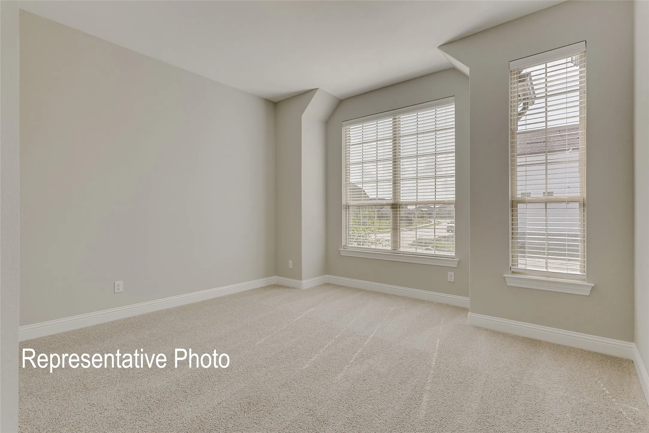 Spacious interior room featuring light-colored carpeting, neutral painted walls, and white baseboards