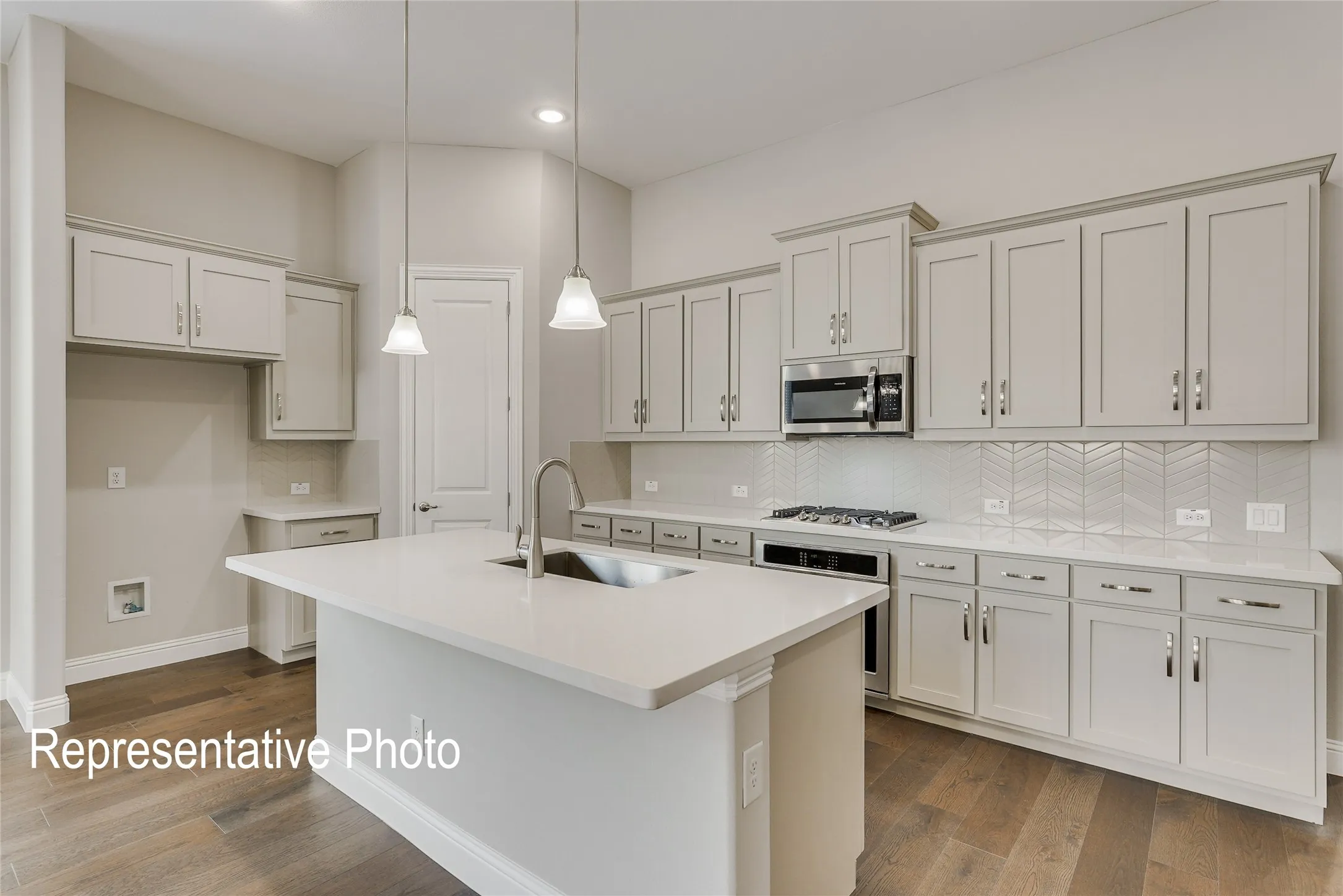 Spacious kitchen featuring a central island with an undermount sink, quartz countertops, light wood-finish flooring, recessed lighting, and a subway tile backsplash with a herringbone pattern