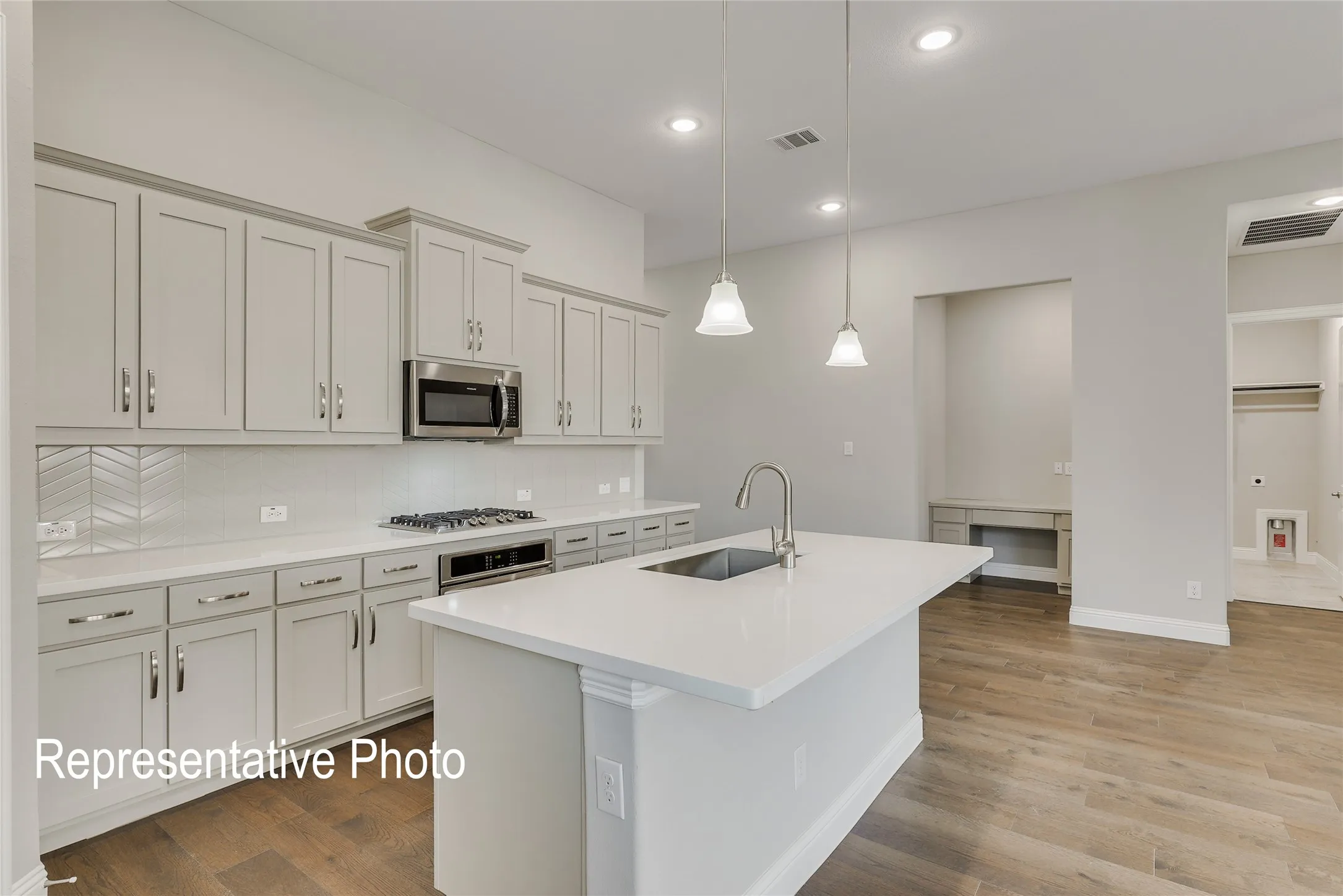 Modern kitchen featuring a central island with an undermount sink, pendant lighting, light-toned cabinetry, stainless steel appliances, and wood-finish flooring