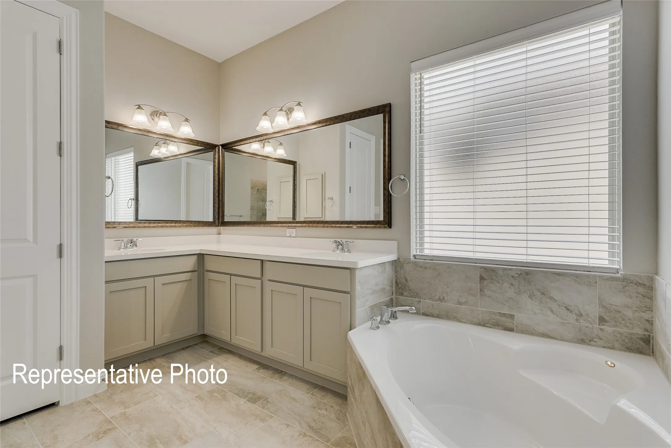 Corner built-in tub with tile surround, dual vanity with undermount sinks, framed mirrors, and overhead vanity lighting