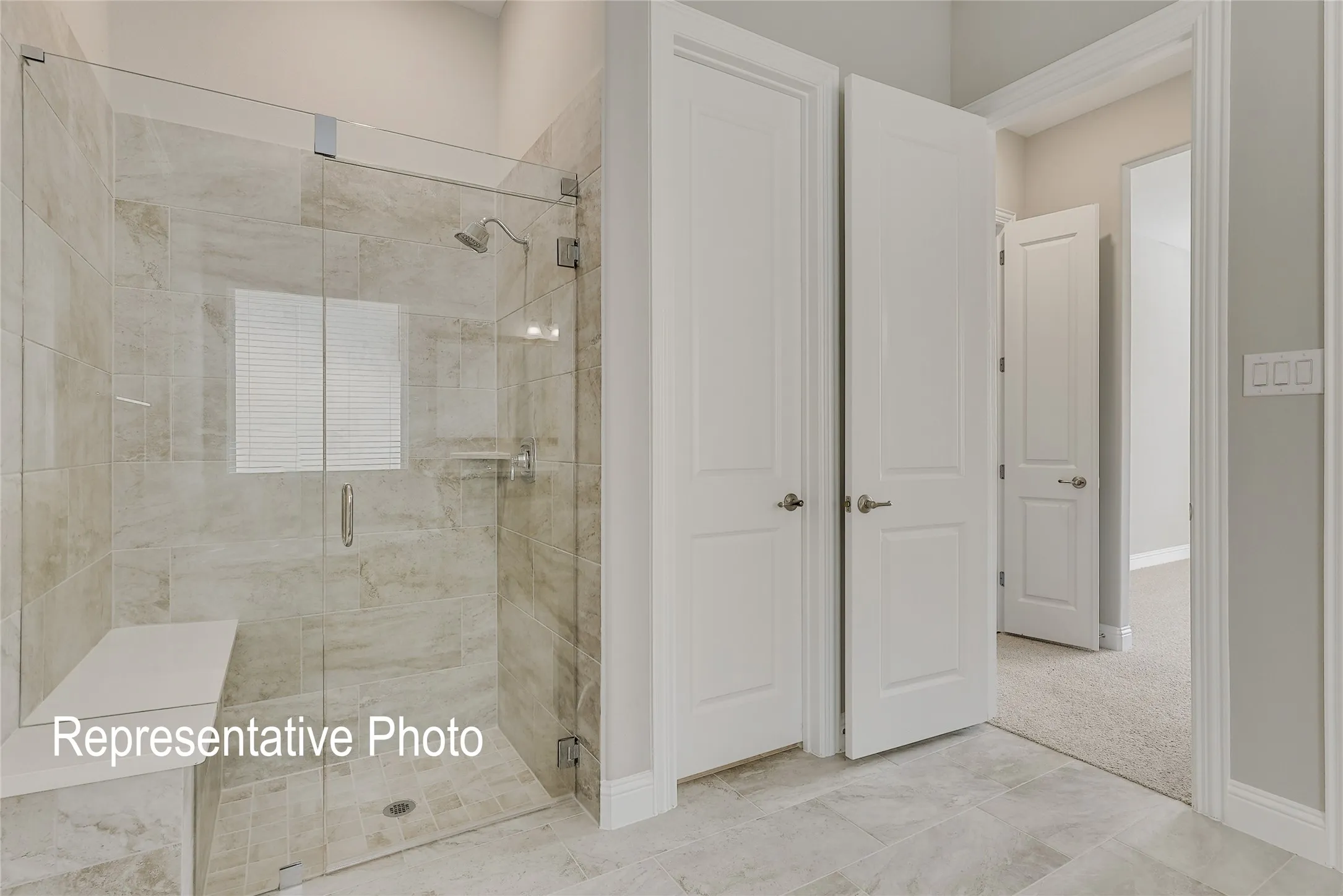 Spacious shower enclosure featuring a frameless glass door, stone-finish tile surround, built-in bench, and a brushed nickel showerhead