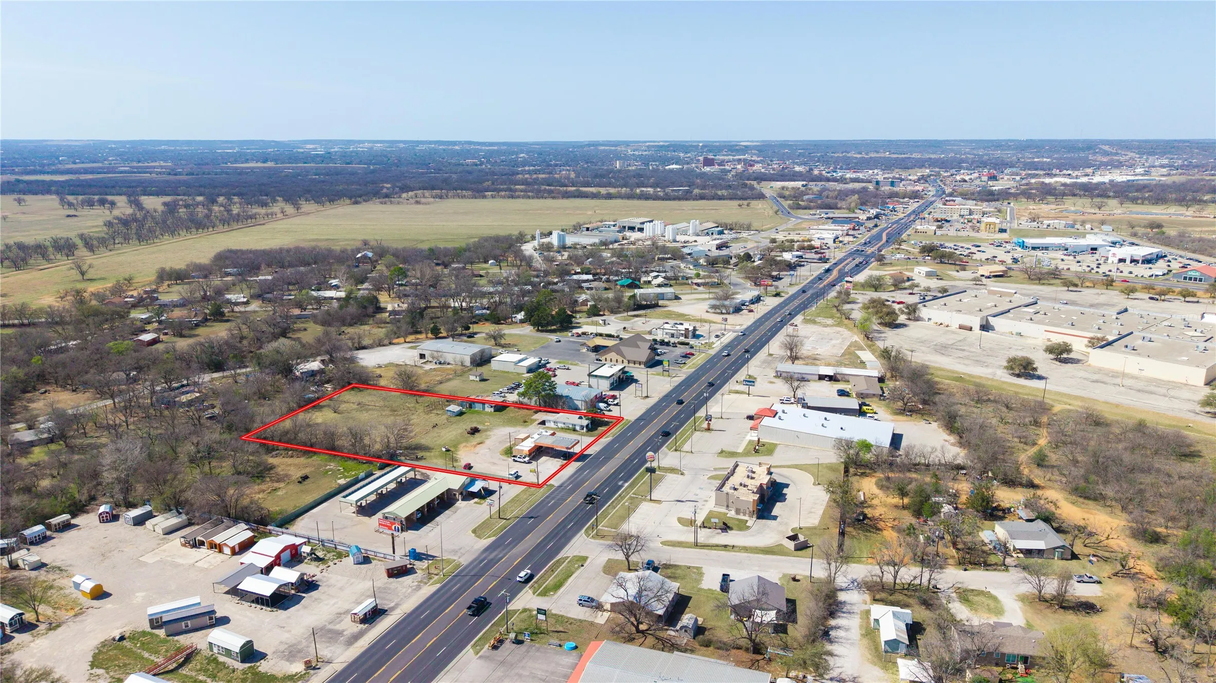 Expansive land parcel with direct frontage on a multi-lane roadway, featuring a rectangular boundary and surrounding commercial structures