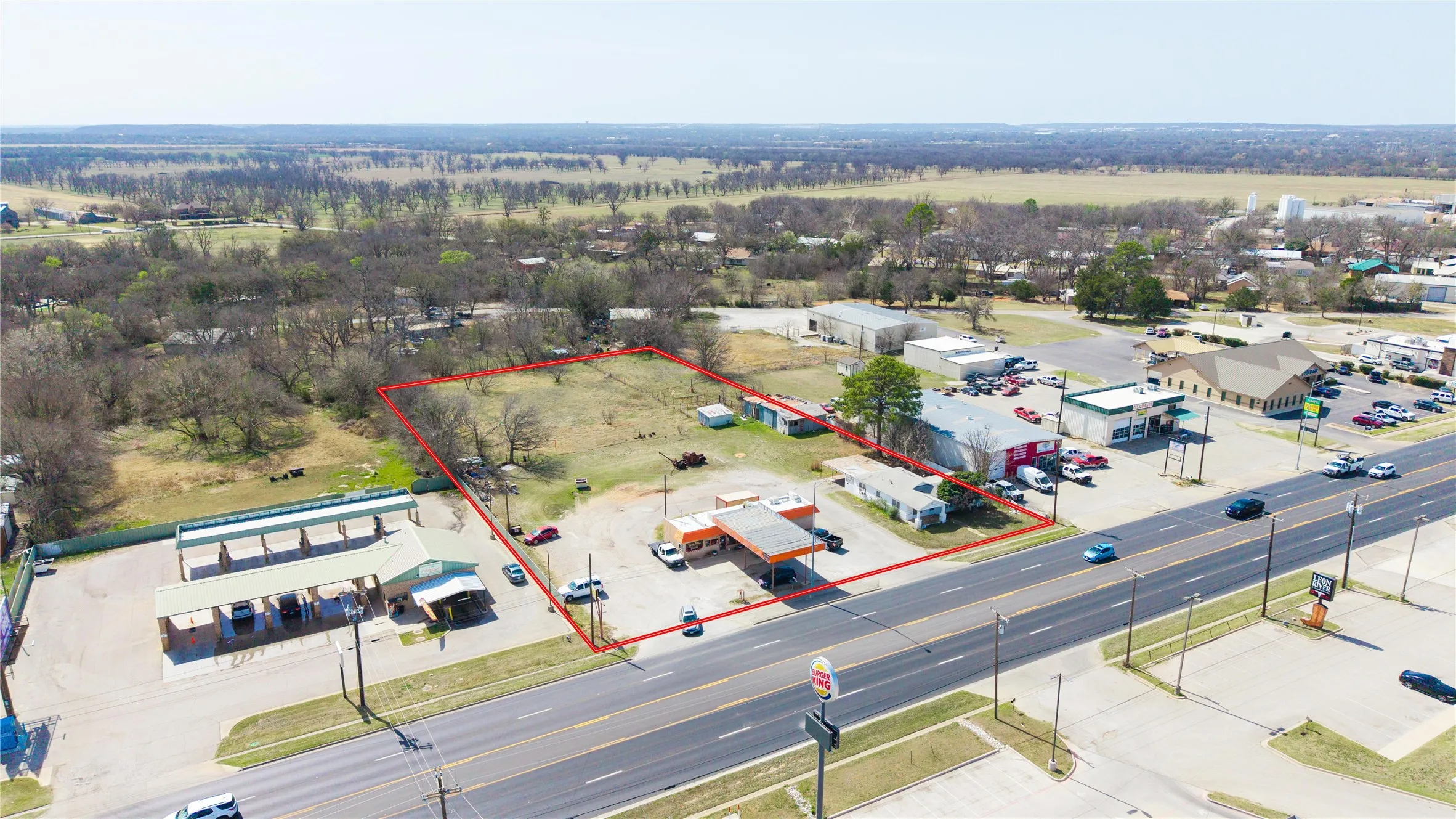 Aerial view of a commercial property featuring a gas station with multiple pumps, an adjacent building, and a substantial undeveloped land parcel