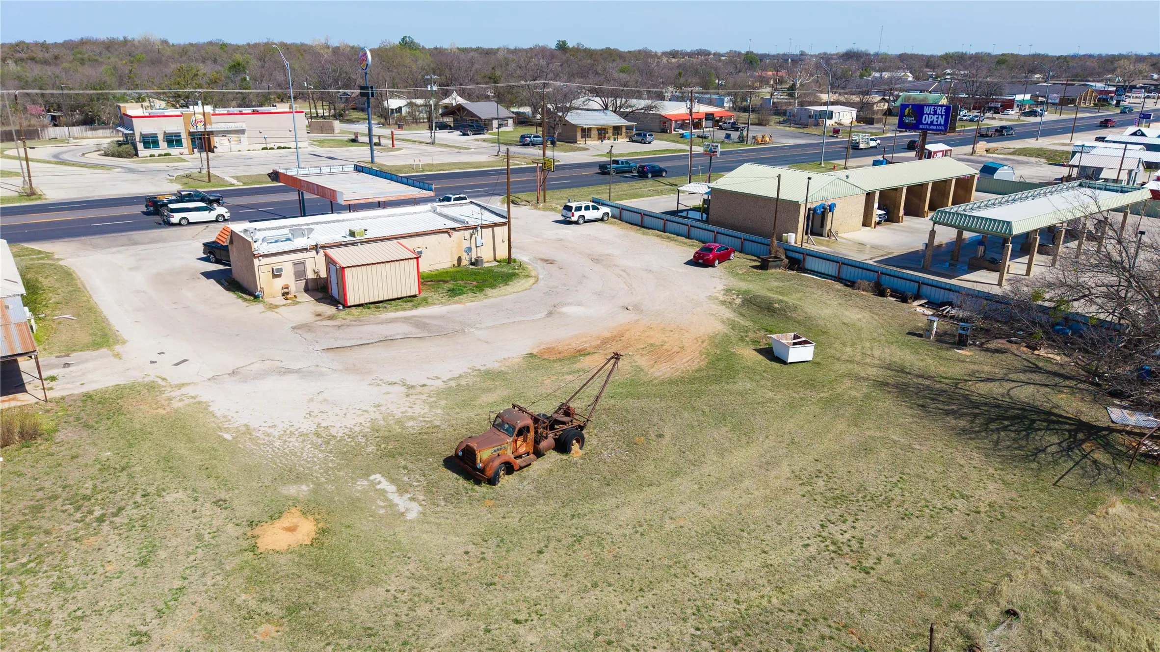 Expansive paved lot with direct road access, featuring a commercial building with an attached canopy structure and a separate multi-bay car wash facility