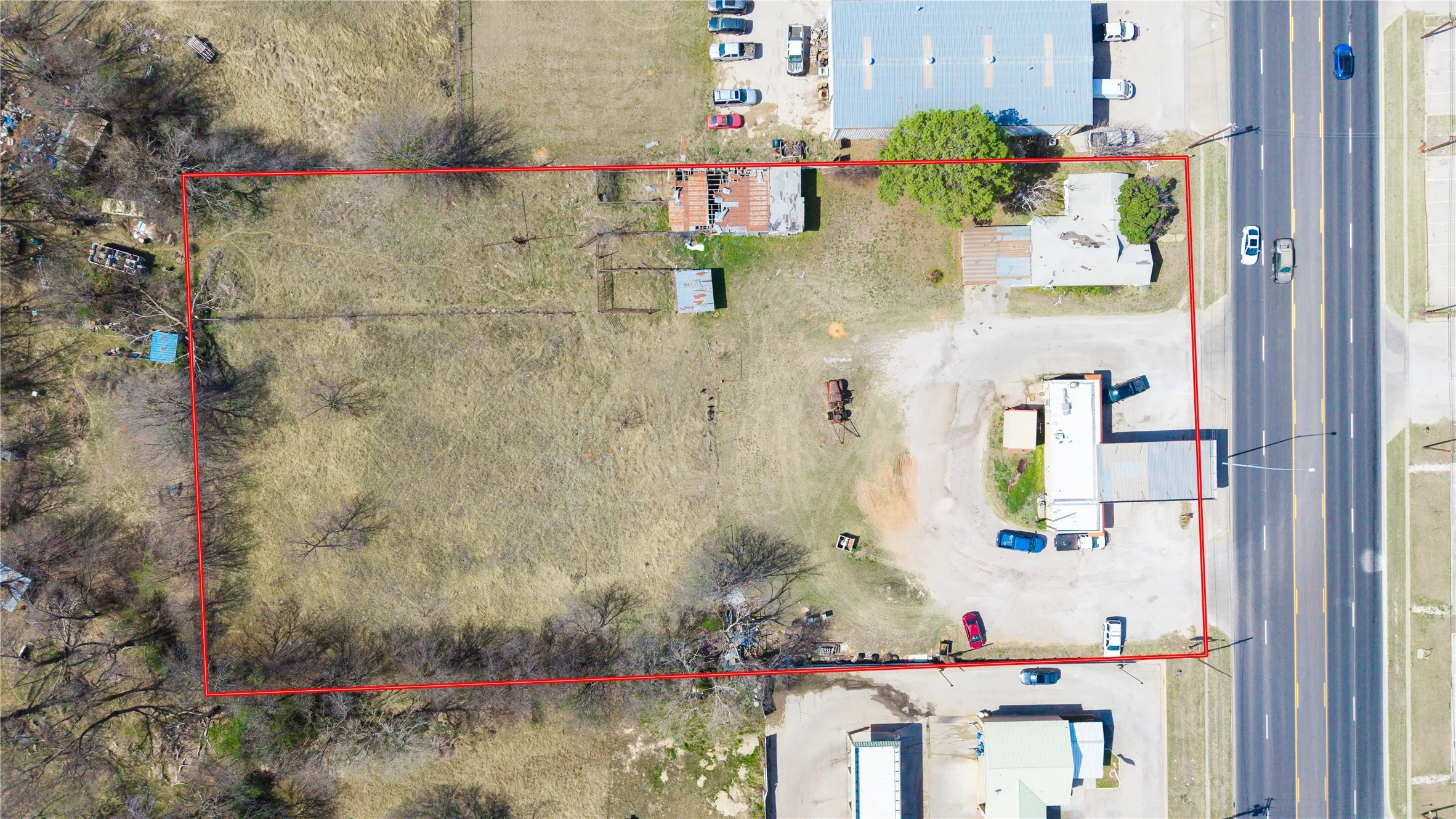 Expansive commercial lot featuring a primary building with an attached covered area, a secondary structure, paved parking areas, and direct frontage on a multi-lane road