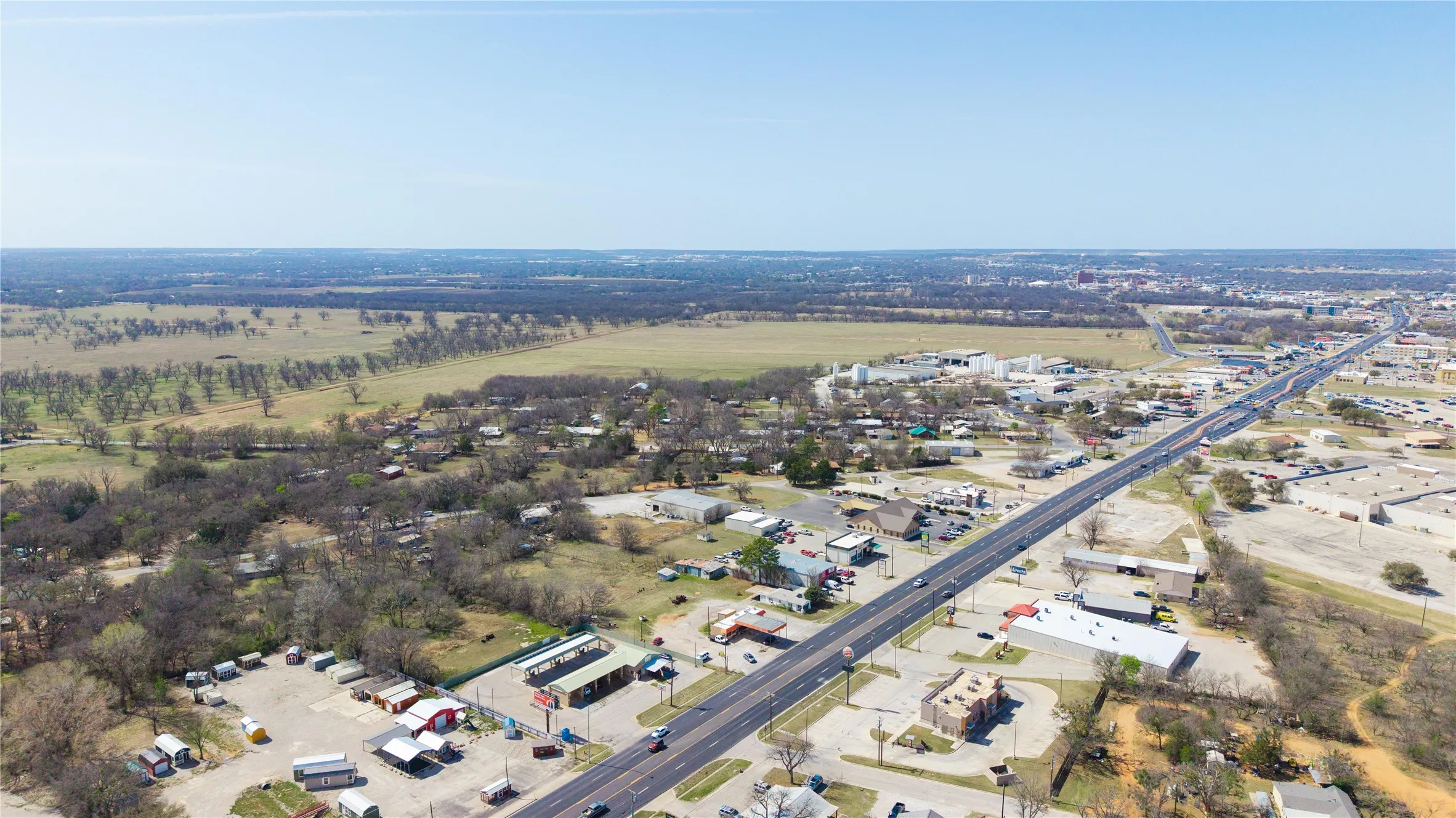 Aerial perspective showcasing an expansive undeveloped land parcel, surrounding commercial properties, a multi-lane highway, and distant structures
