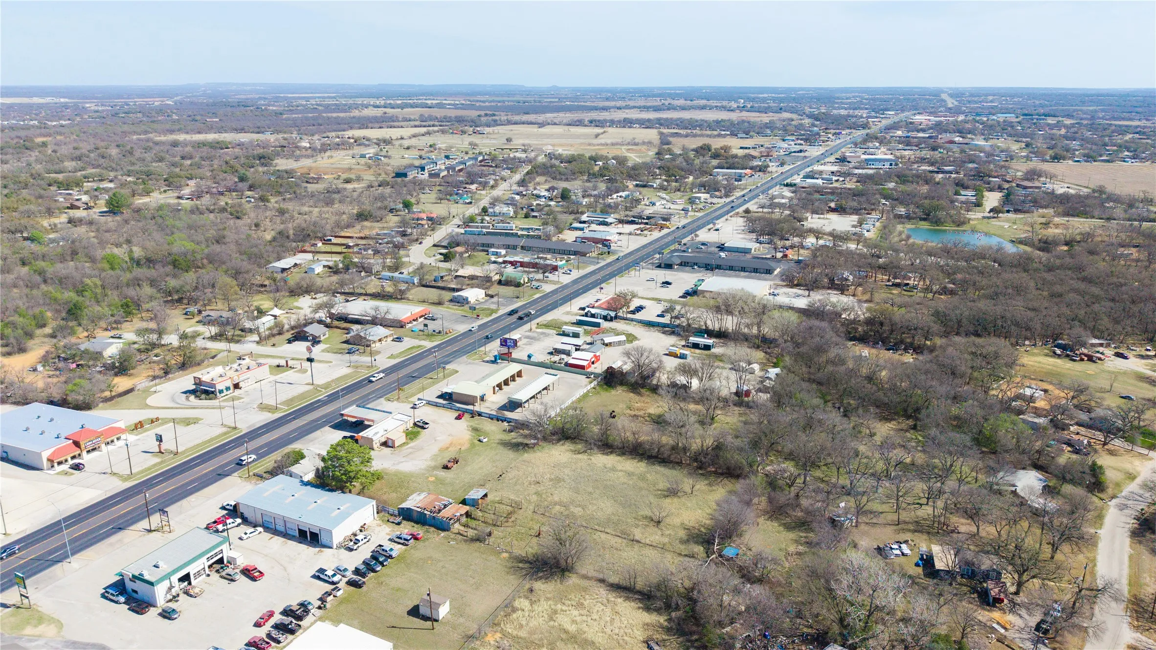 Aerial perspective of a commercial corridor featuring a multi-lane roadway, various commercial structures, and undeveloped land