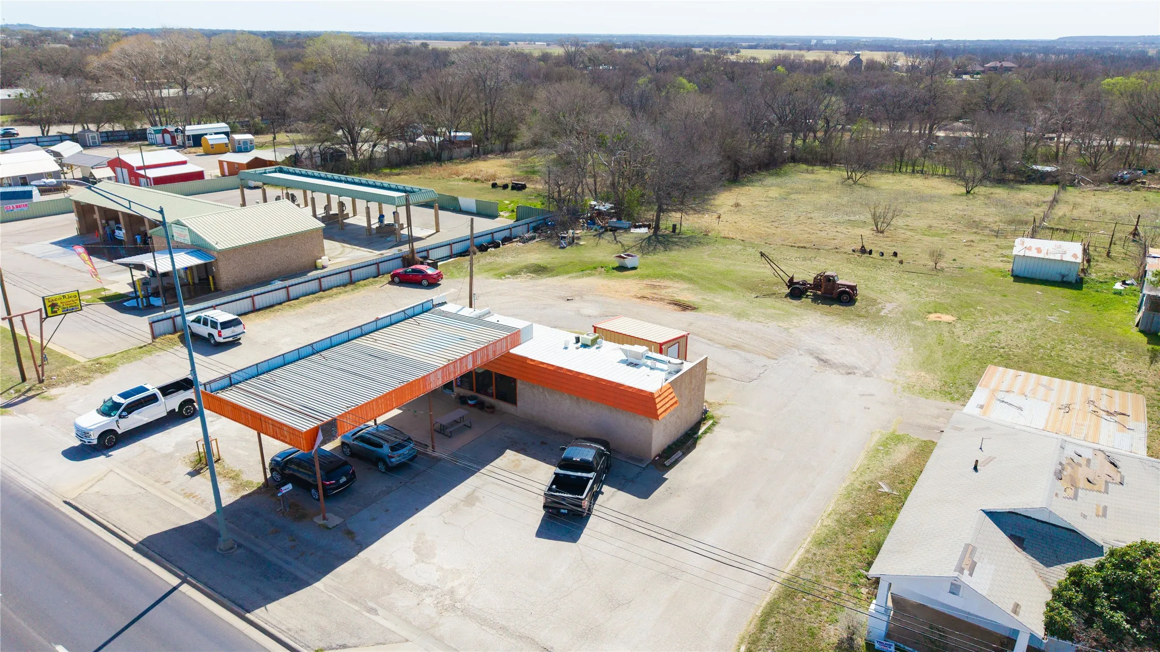Commercial property featuring two distinct building structures, extensive paved lot space, and multiple covered parking/service areas