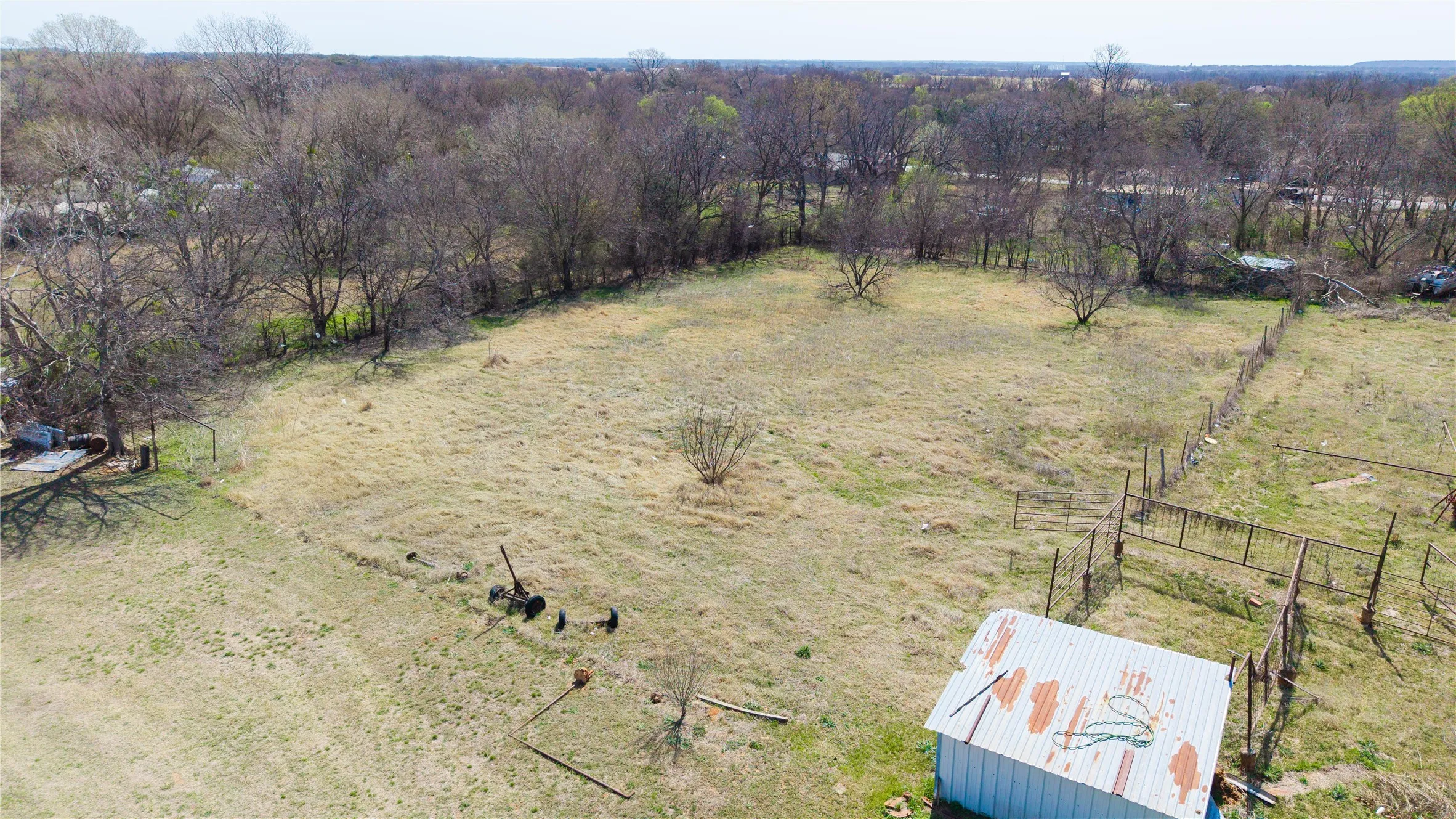 Expansive open lot featuring a perimeter fence, mature trees, and a detached outbuilding with a metal roof