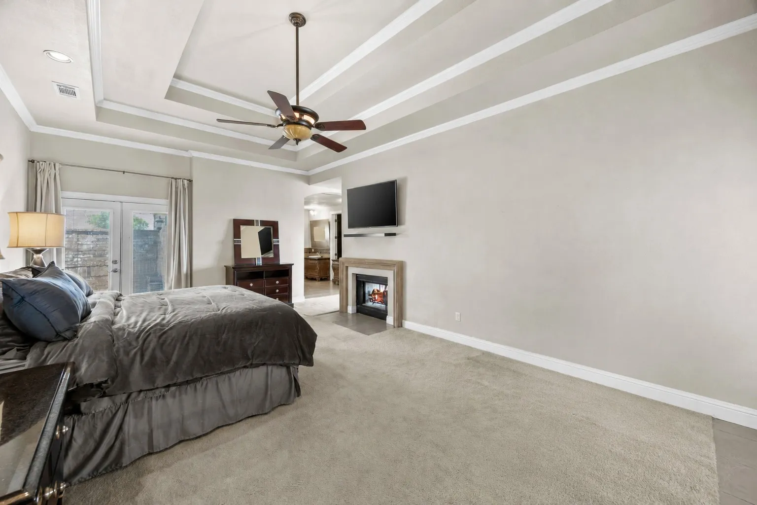 Spacious primary suite featuring tray ceilings, oversized layout, private patio/courtyard access, & a peaceful retreat-like atmosphere.