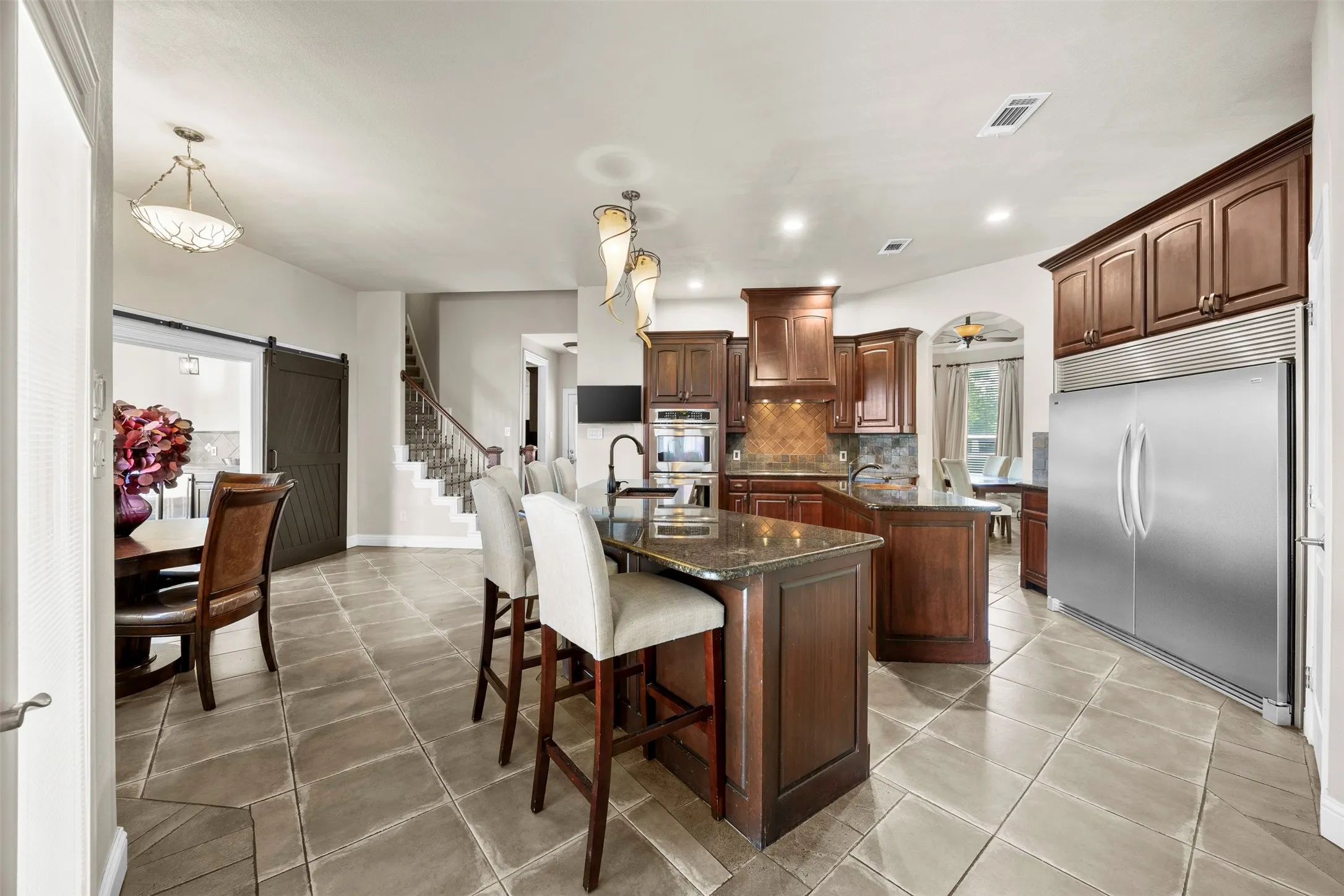 Chef’s kitchen designed for entertaining with double ovens, oversized island seating, built-in refrigerator/freezer, walk-in pantry, hidden microwave, abundant prep space, & open flow into the breakfast nook and main living areas