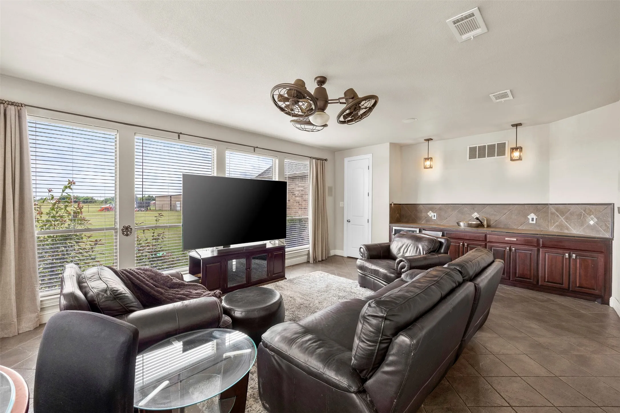 Oversized flex space off the kitchen with wall-to-wall windows, backyard access, built-in serving bar, mini fridge, ice maker, convenient half bath, & endless possibilities for a game room, family room, man cave, or entertaining space.