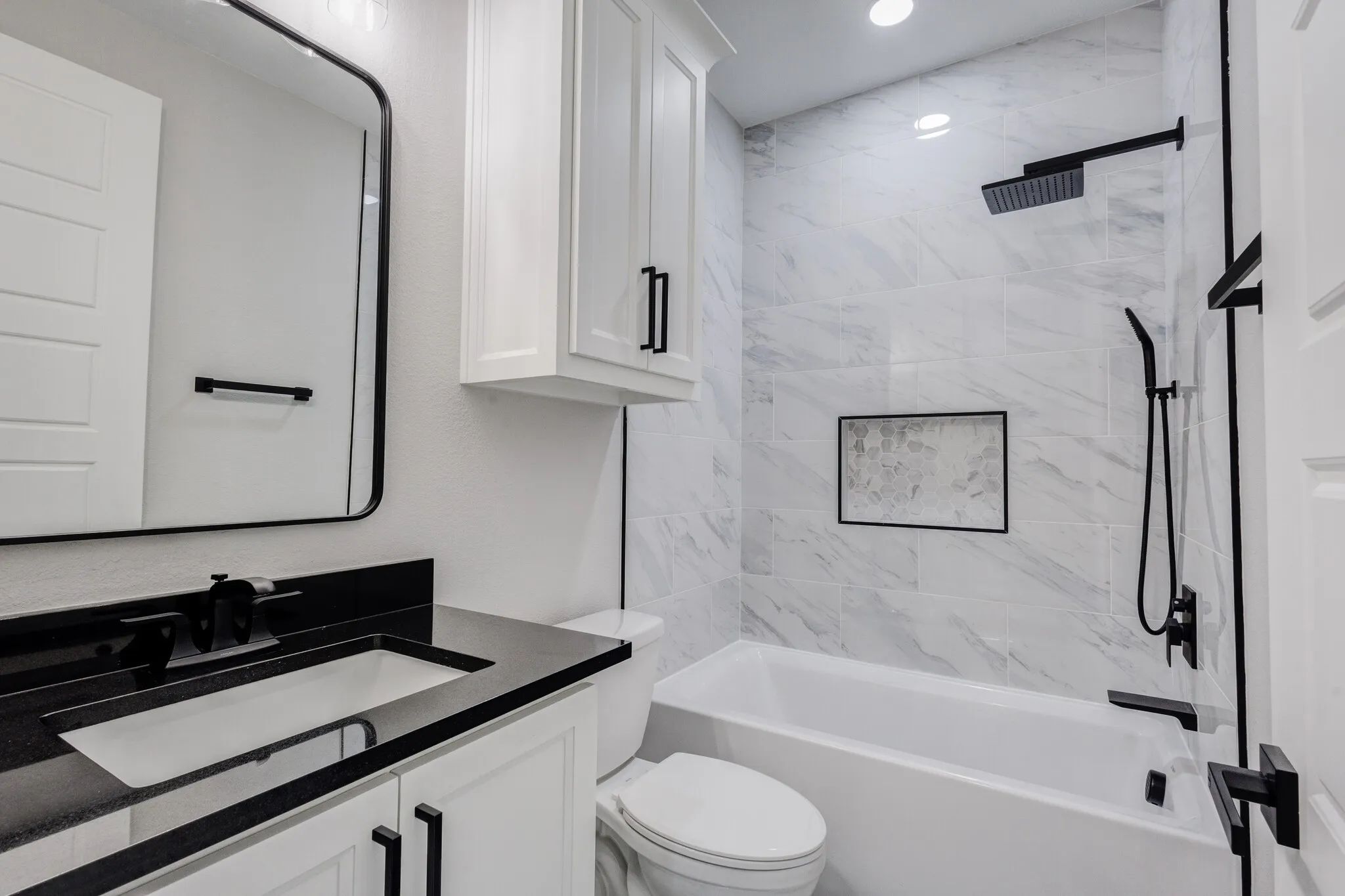 Bathroom featuring a tub/shower combination with white marble-look tile surround and a tiled niche