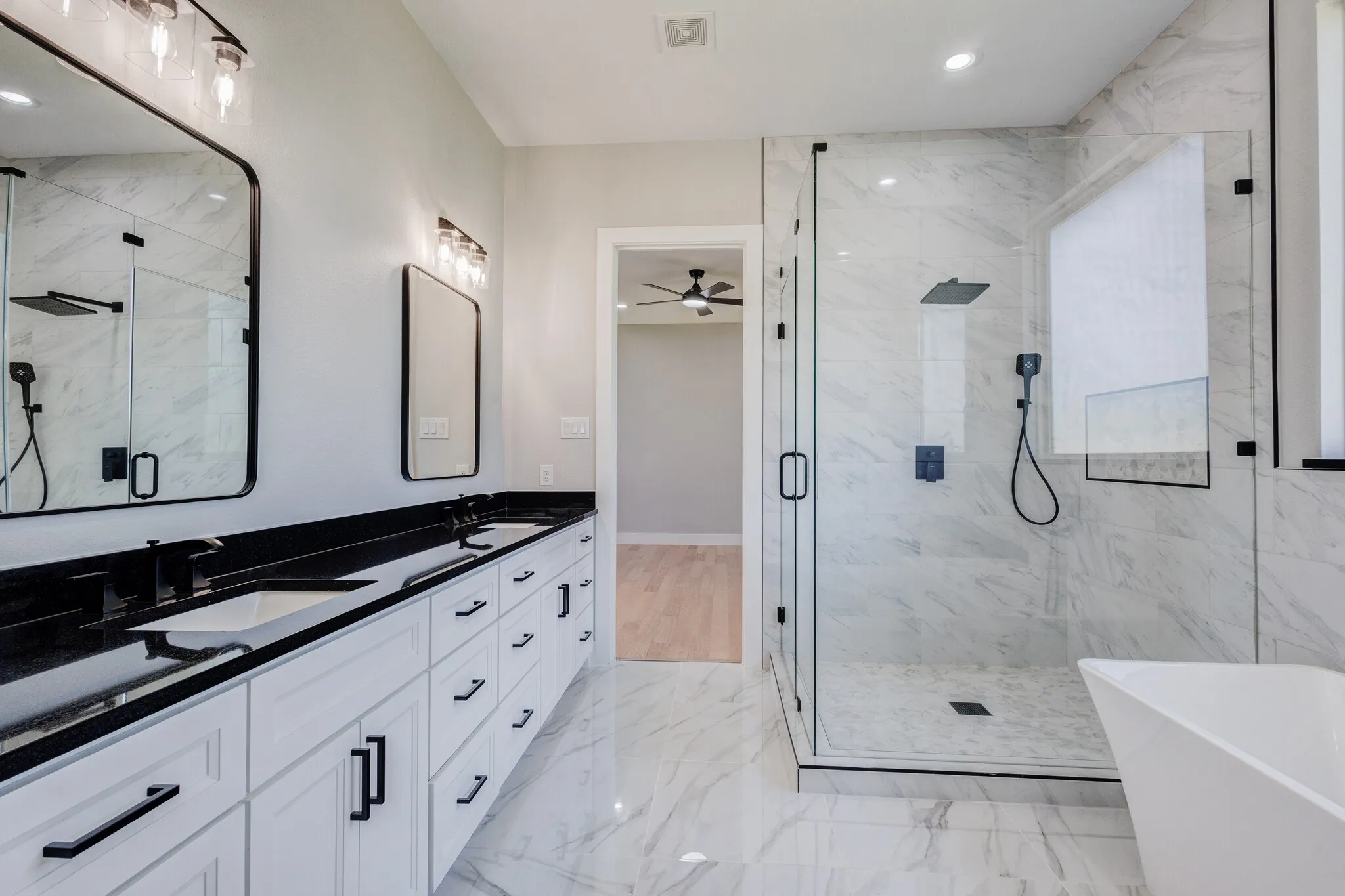 Bathroom featuring a double vanity with white cabinetry and black countertops, dual rectangular sinks, and matte black hardware