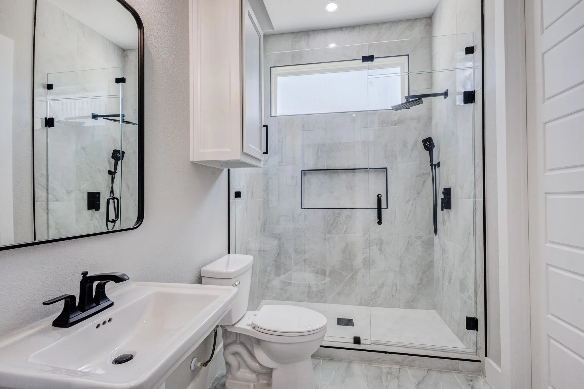 Walk-in shower with clear glass enclosure and black hardware, featuring a rainfall showerhead and separate handheld sprayer