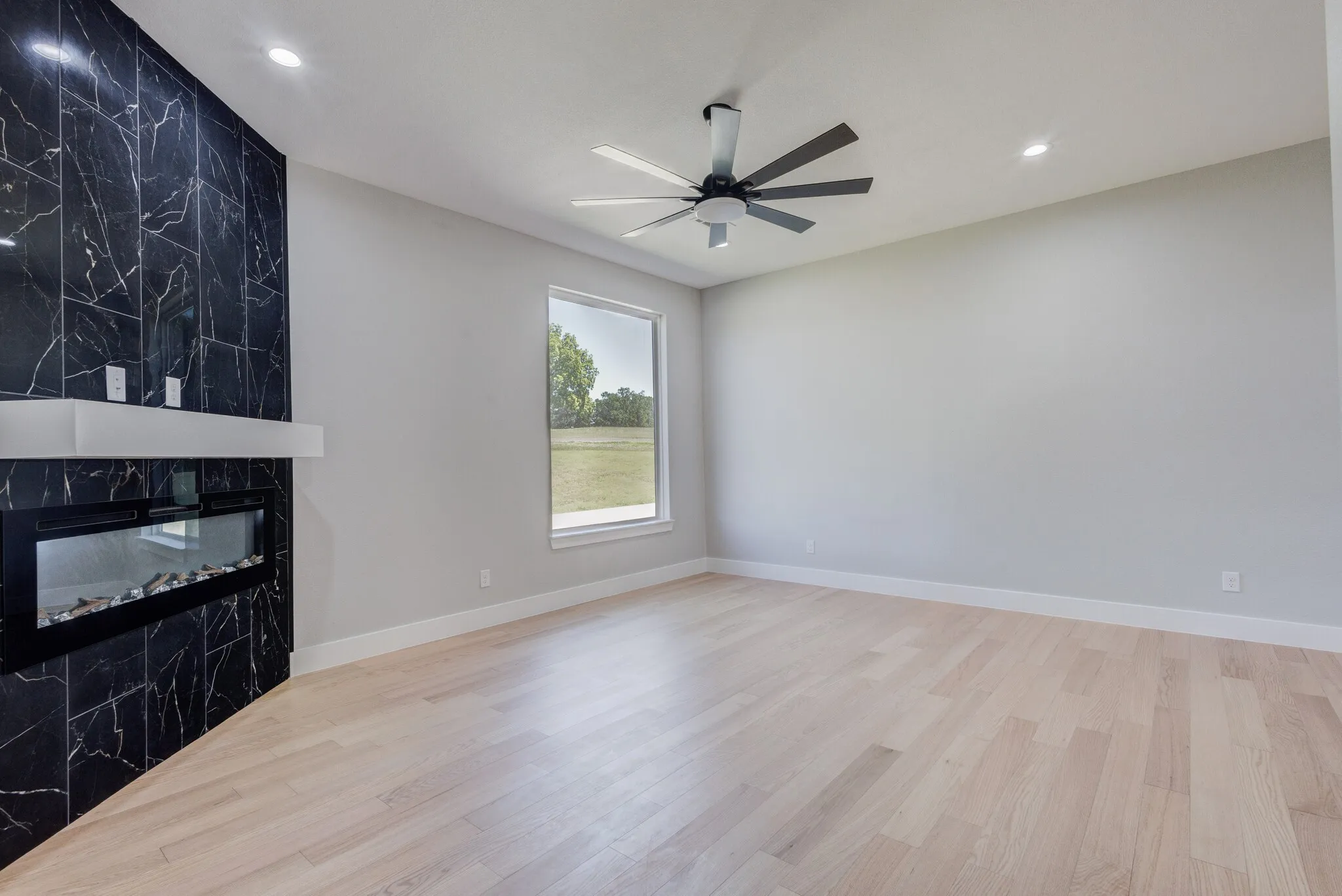 Feature wall with dark tile surround and integrated linear fireplace, light wood-finish flooring, recessed lighting, ceiling fan, and a large window