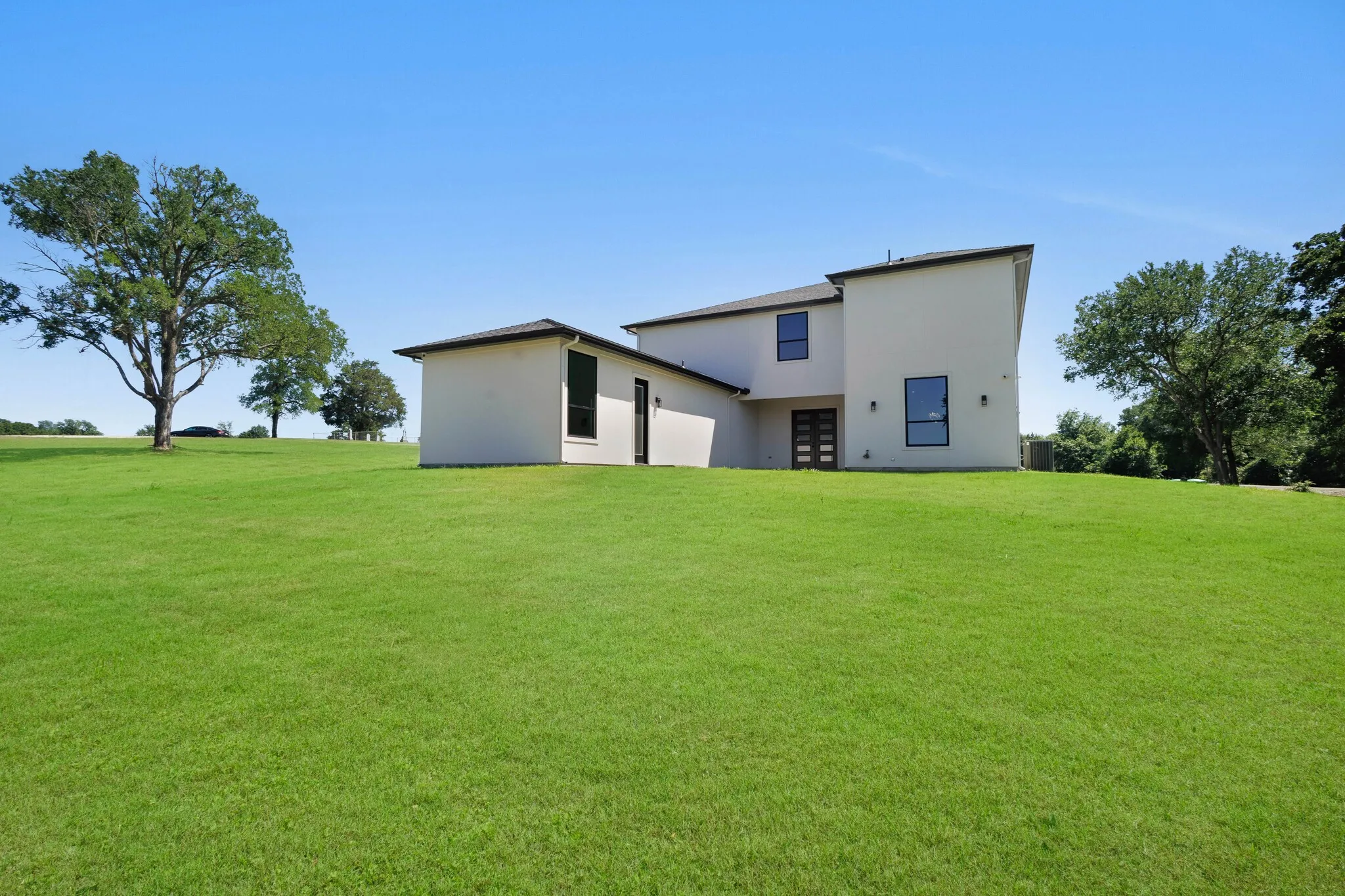 Contemporary stucco exterior with a multi-level design, featuring black-framed windows, a dark multi-pane entry door, and recessed exterior lighting