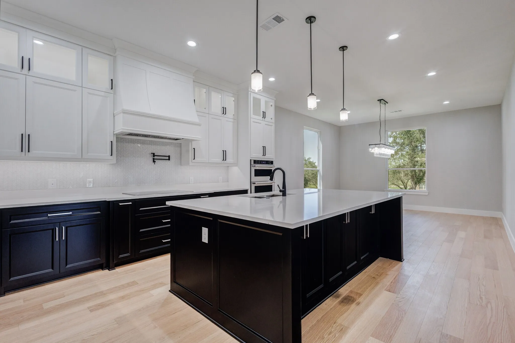 Open-concept kitchen featuring an expansive central island with a sink, white countertops, two-tone cabinetry, wood-finish flooring, and recessed lighting