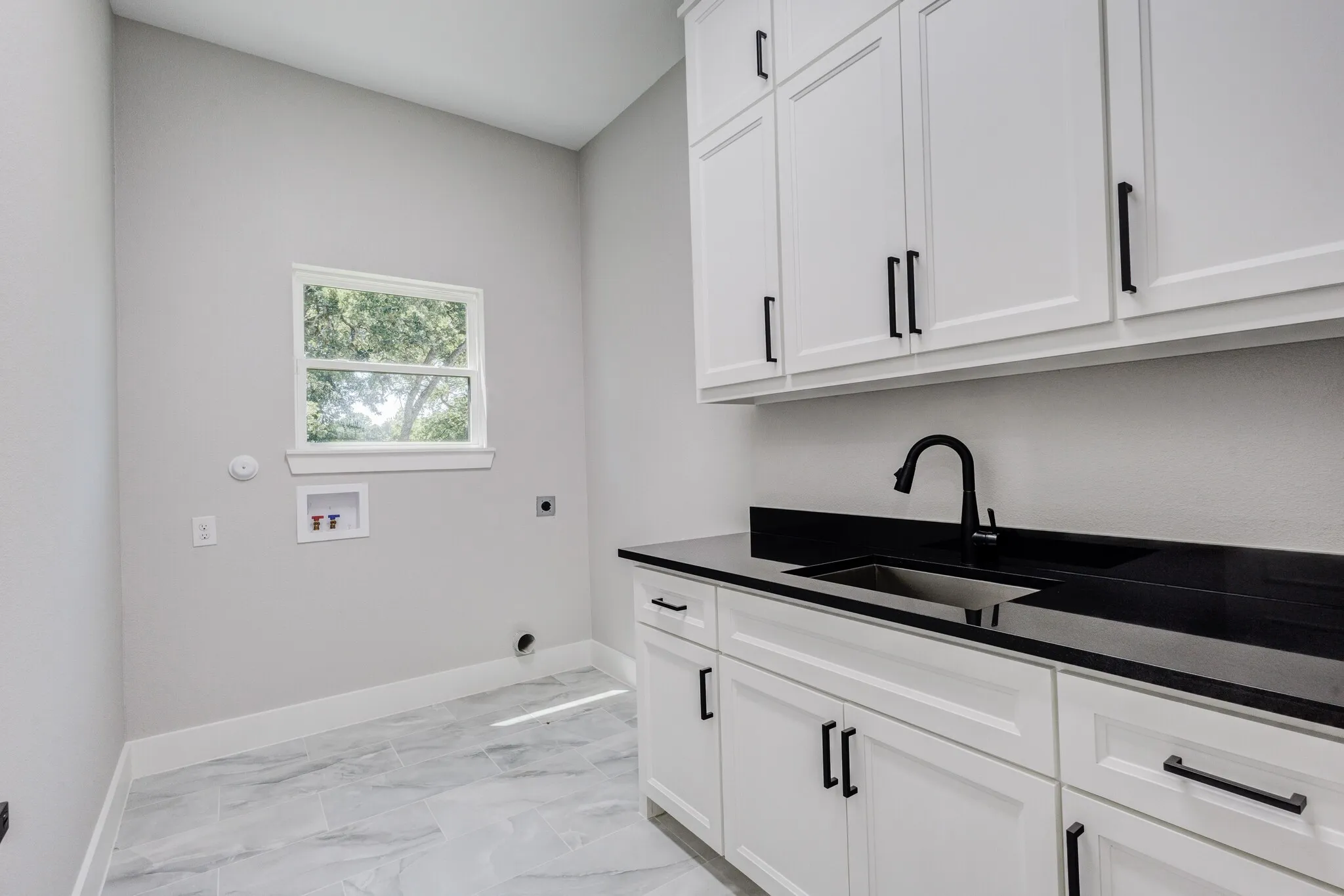 Laundry room featuring white cabinetry with black hardware, a black countertop, and an undermount sink with a matte black faucet