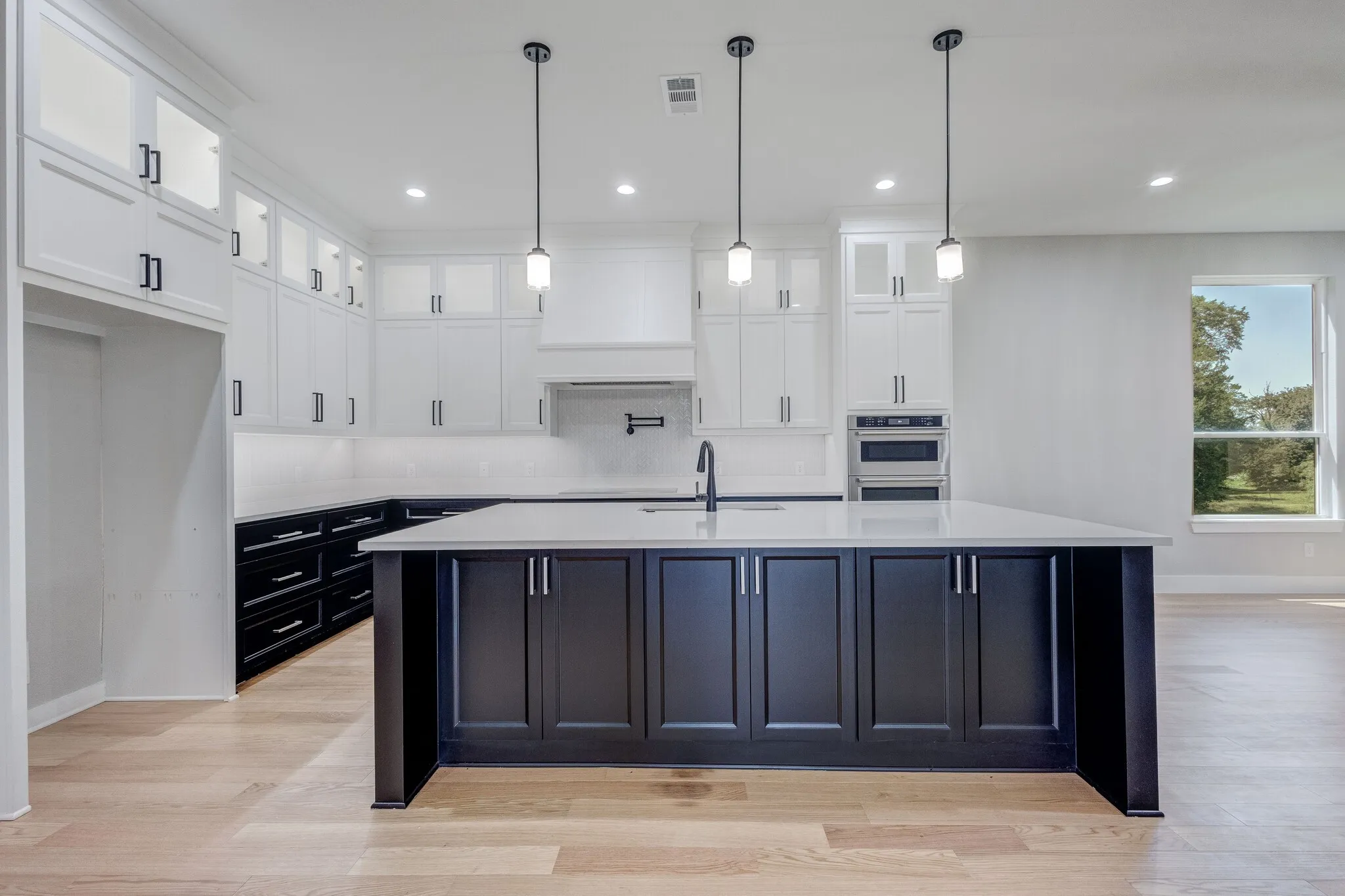 Contemporary kitchen featuring a large central island with dark cabinetry, complemented by white upper and dark lower perimeter cabinetry