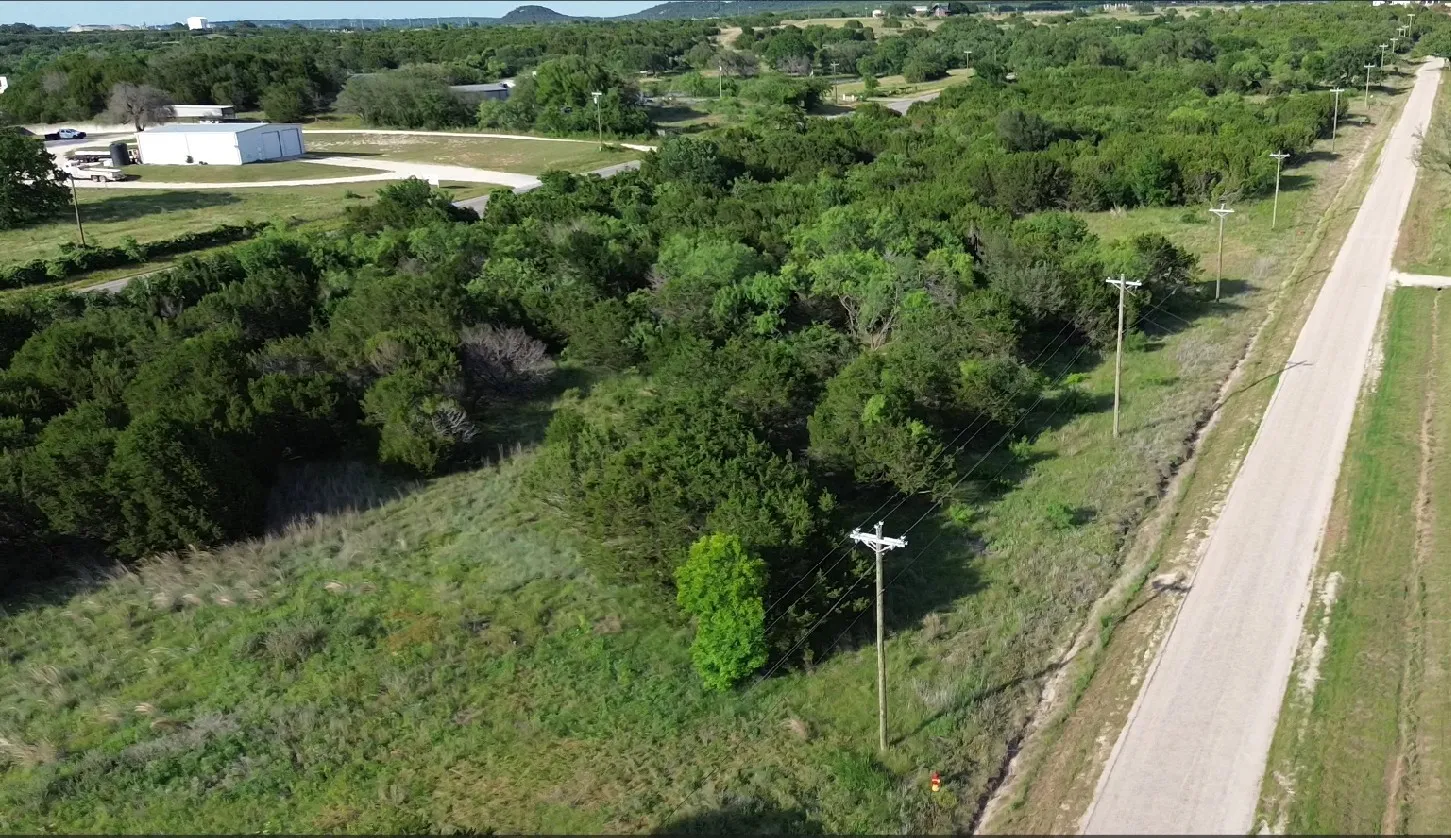 Expansive undeveloped land featuring a paved roadway, mature trees, and overhead utility lines. Displays Portions of lot# 96-98
