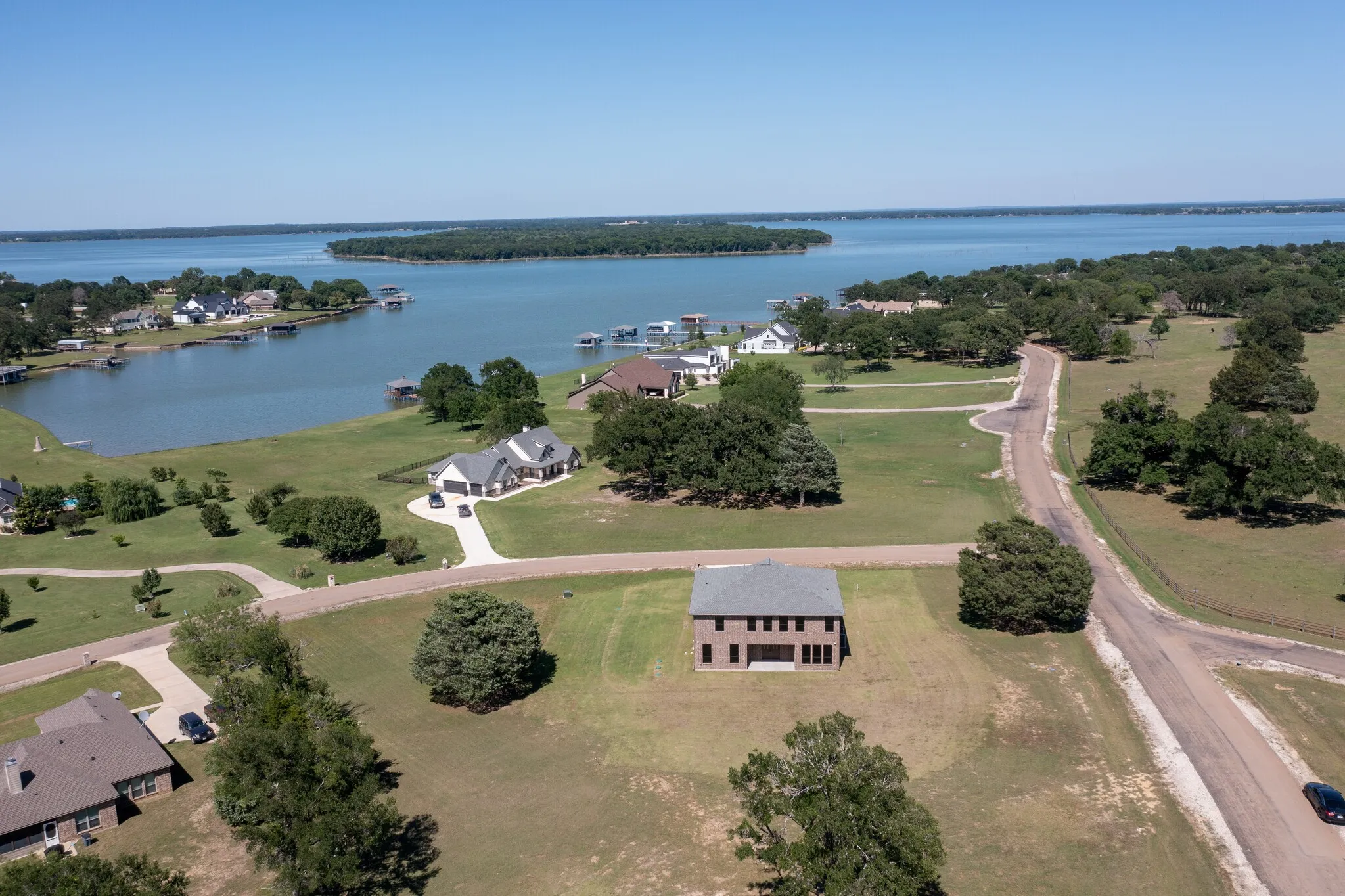 Expansive waterfront property featuring a two-story brick residence with multiple windows, a stone-colored shingled roof, and a concrete driveway