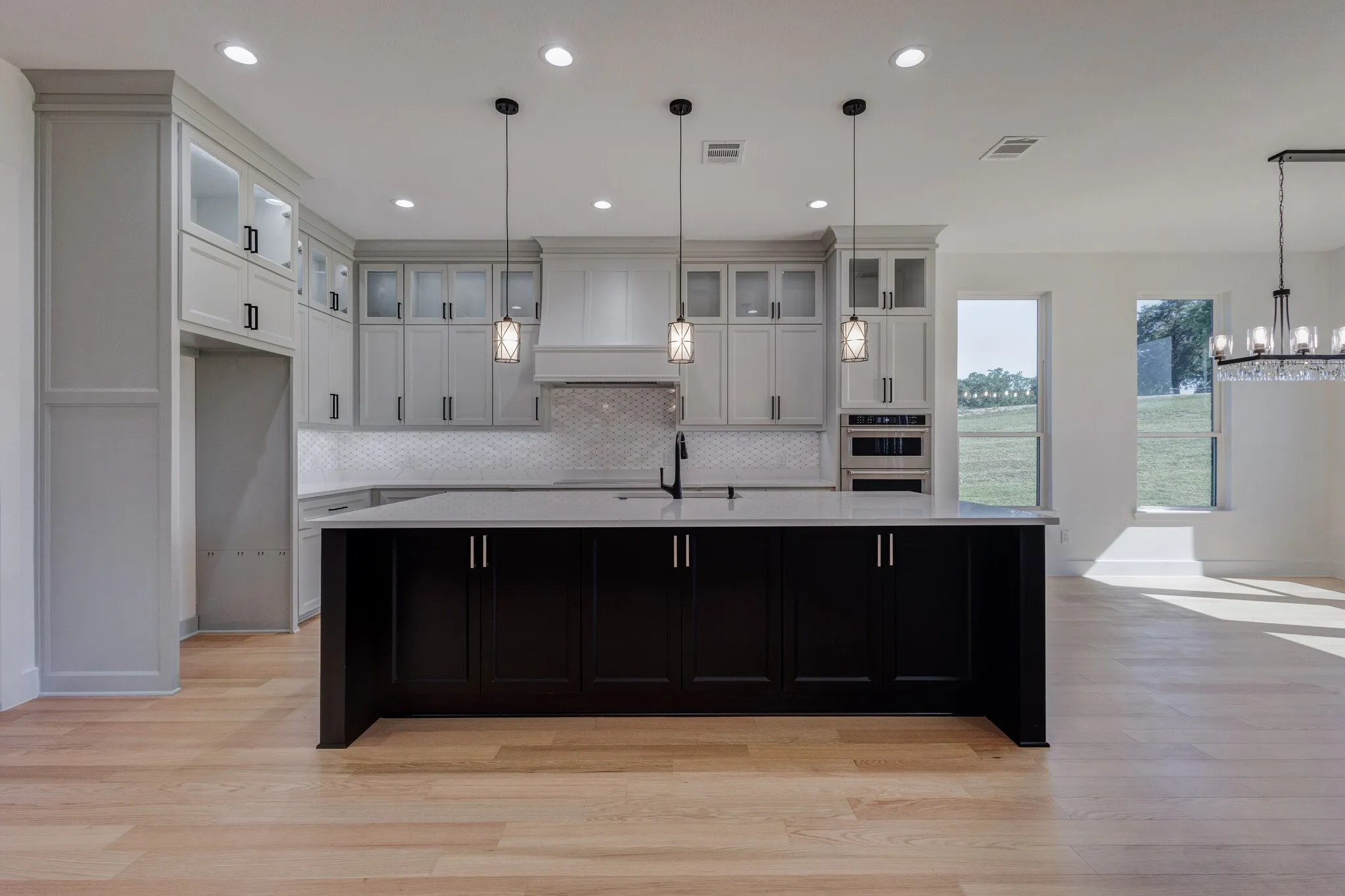 Modern kitchen featuring a large central island with dark cabinetry, light wood-finish flooring, and recessed ceiling lighting