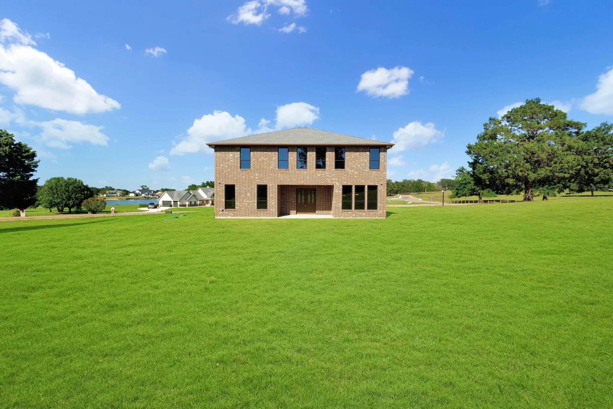 Two-story brick exterior residence featuring a gray shingled roof and multiple windows with dark frames