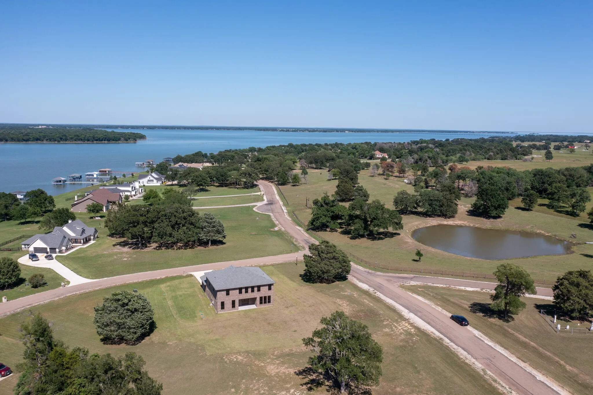 Expansive waterfront property featuring a substantial body of water, green landscape, surrounding trees, and a visible road network