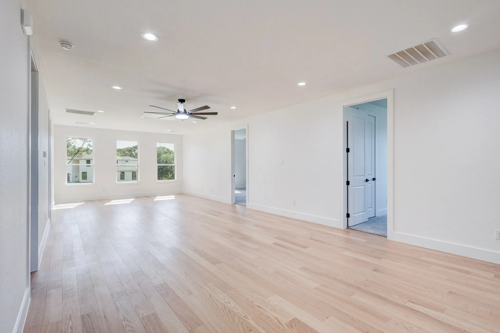 Spacious room featuring light wood-finish flooring, recessed lighting, and a contemporary ceiling fan