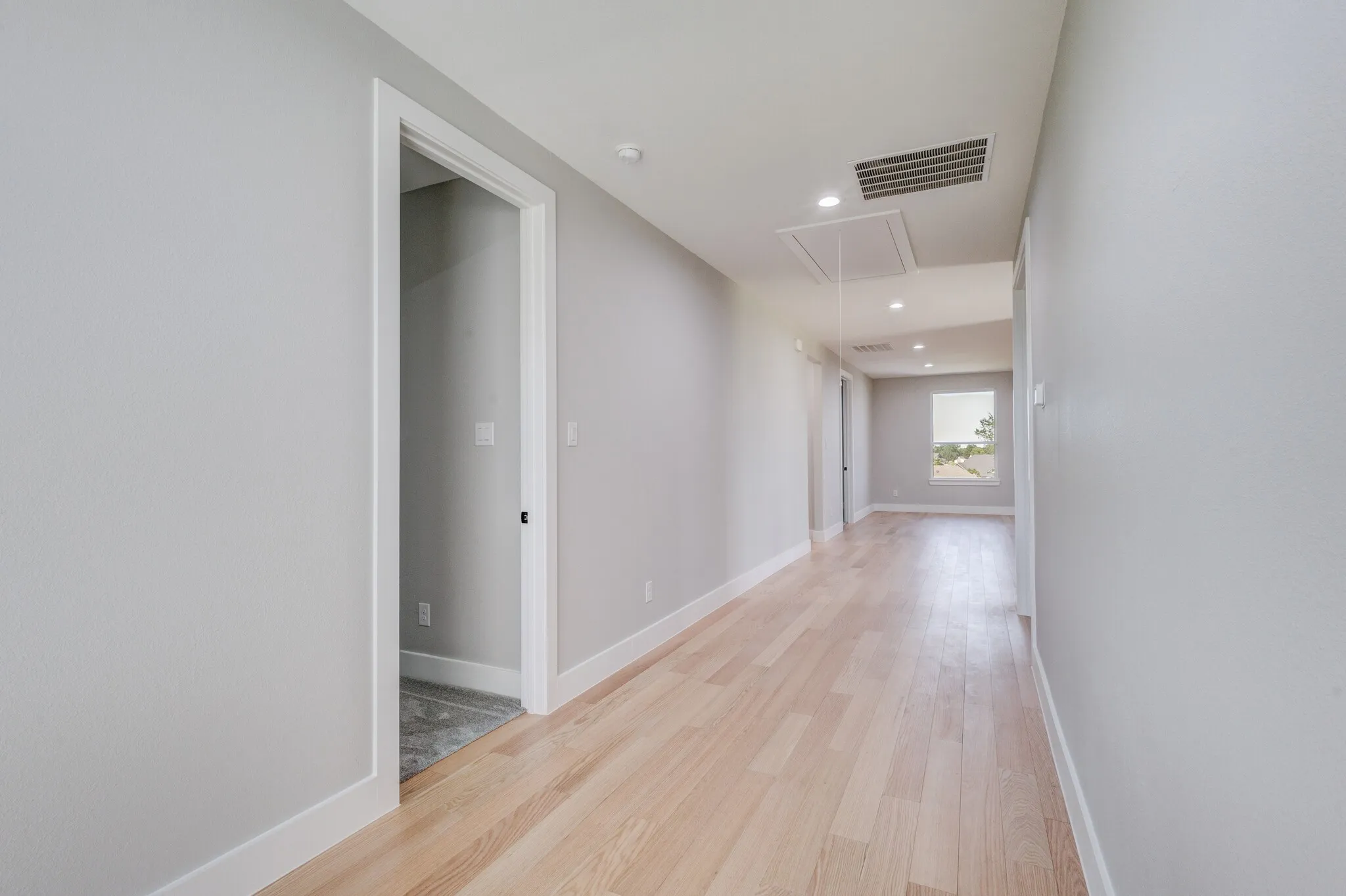 Hallway with light wood-finish flooring, light grey painted walls, white baseboards, and white door casings