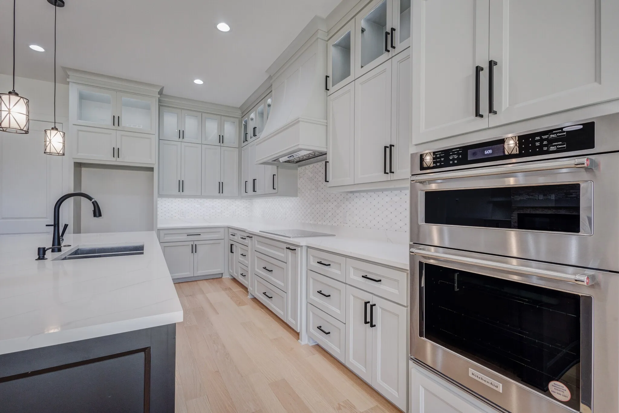 Kitchen featuring light wood-finish flooring, white perimeter cabinetry with black hardware, white quartz countertops, and a white geometric tile backsplash