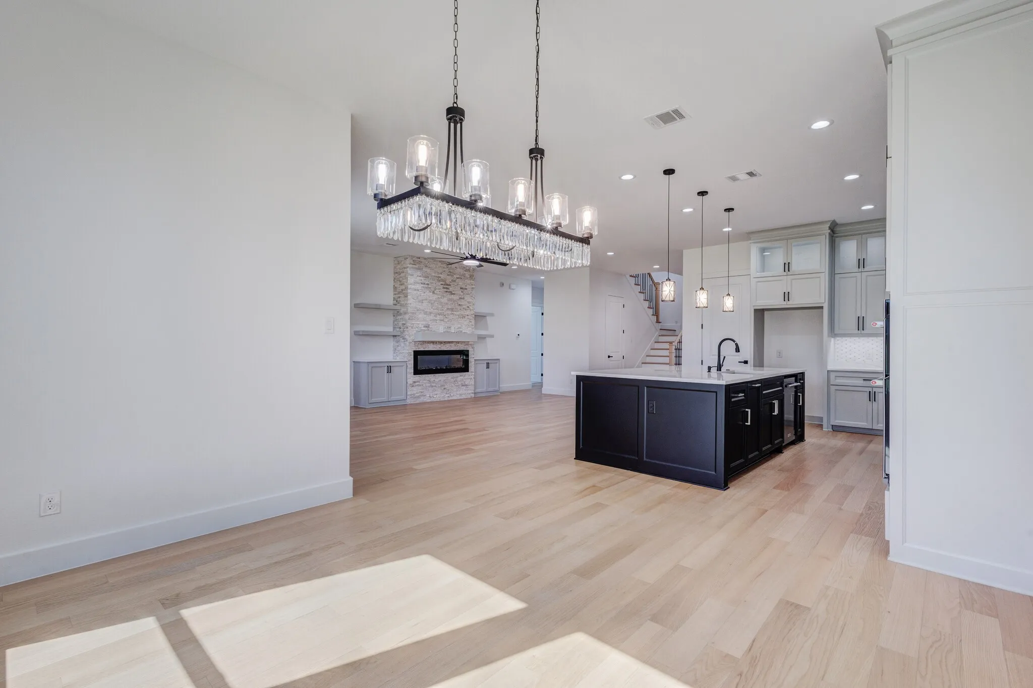 Open-concept living space with light wood-finish flooring, a contemporary linear chandelier, and recessed lighting