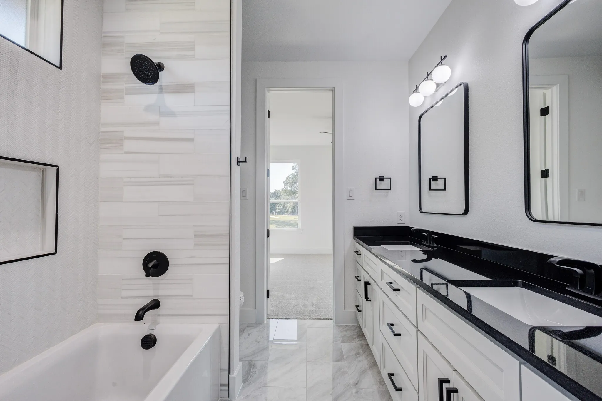 Bathroom featuring a dual vanity with black countertops, white cabinetry, and matte black hardware
