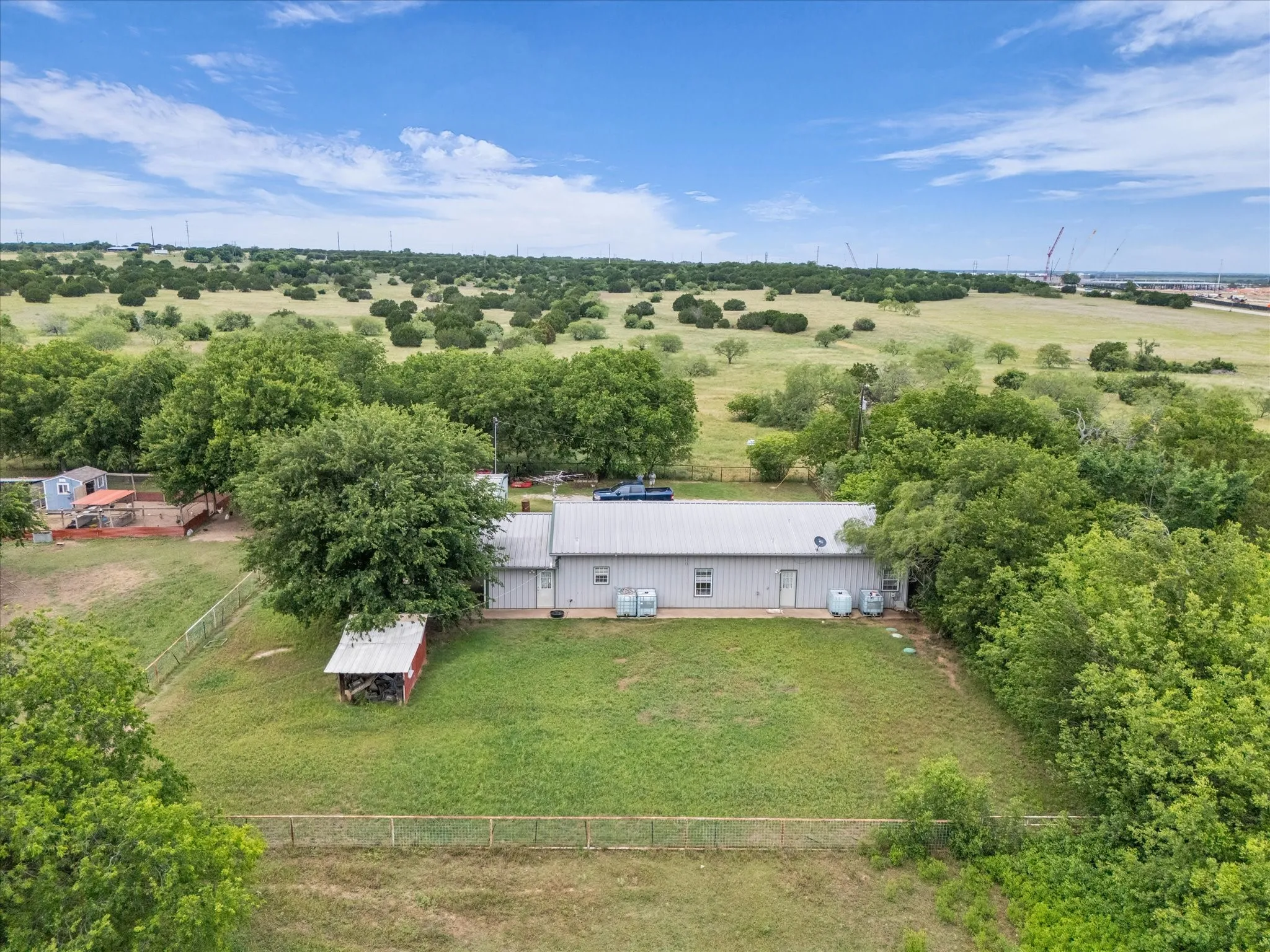 Expansive property featuring a metal-sided structure with a metal roof, surrounded by mature trees and a large grassy area