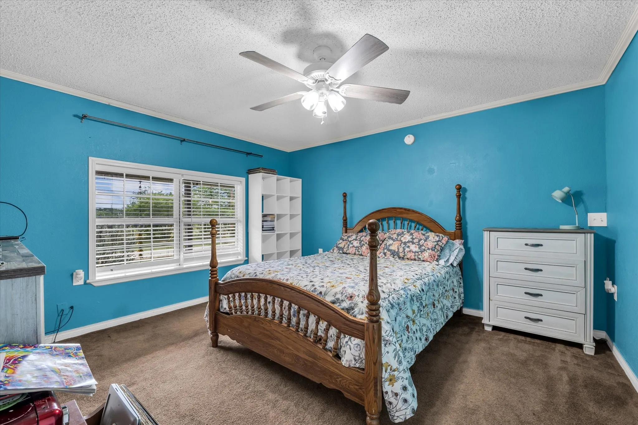 Spacious interior room featuring a multi-pane window with horizontal blinds, built-in shelving, a ceiling fan, and crown molding